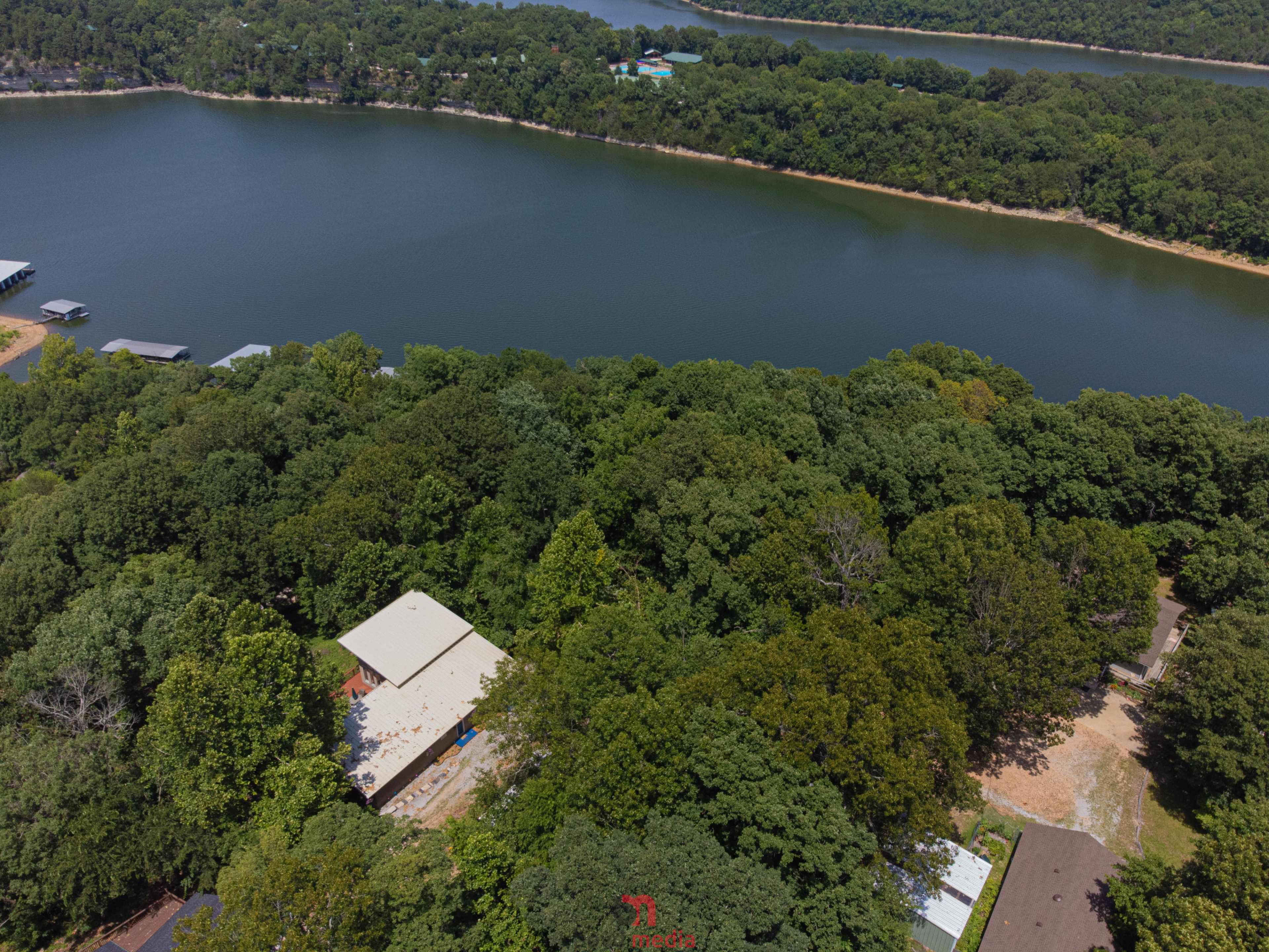 A section of a dense forest surrounding a calm body of water, with a few buildings and docks visible along the shoreline.
