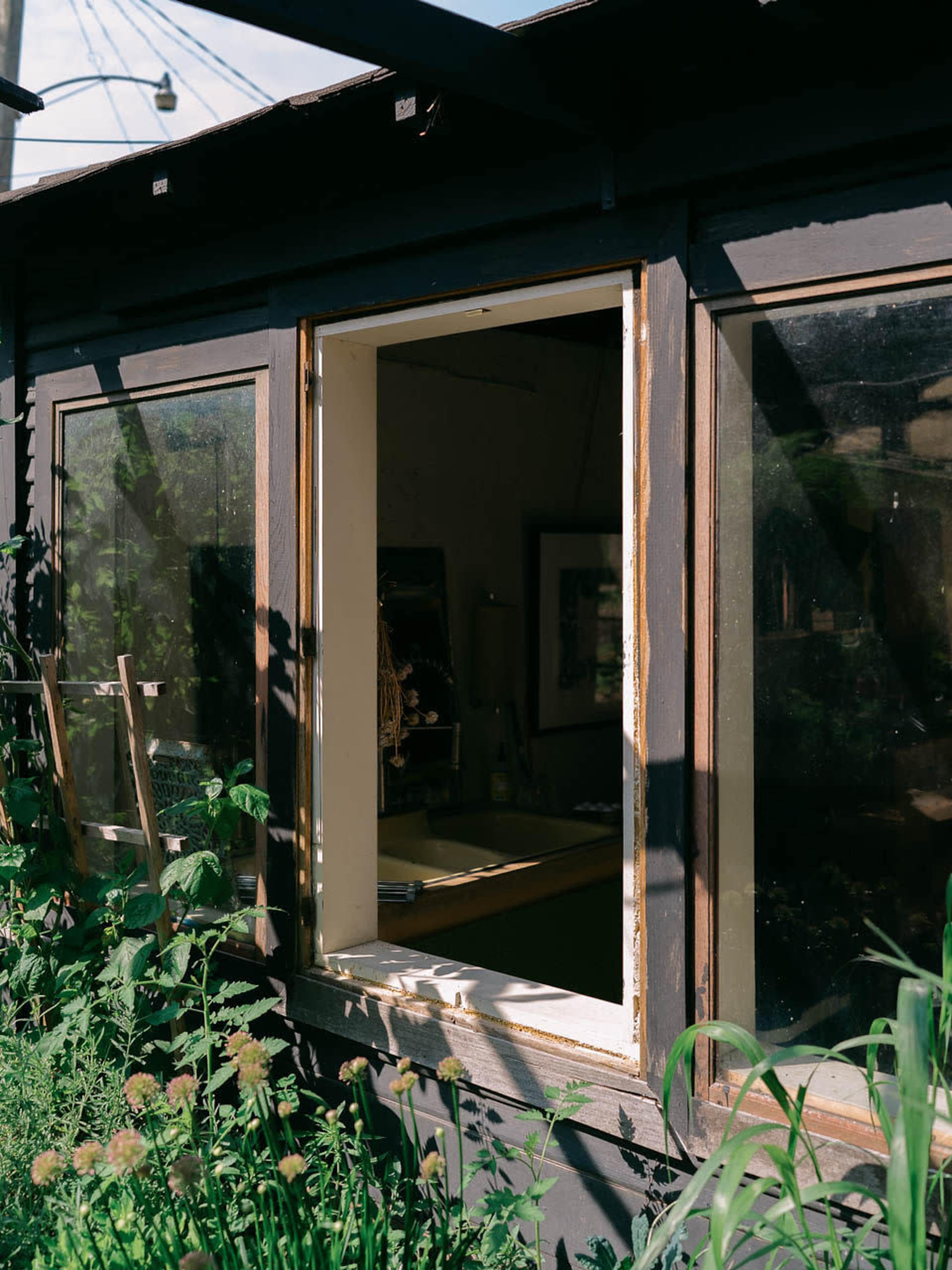 A partially open window reveals an indoor space surrounded by lush greenery.