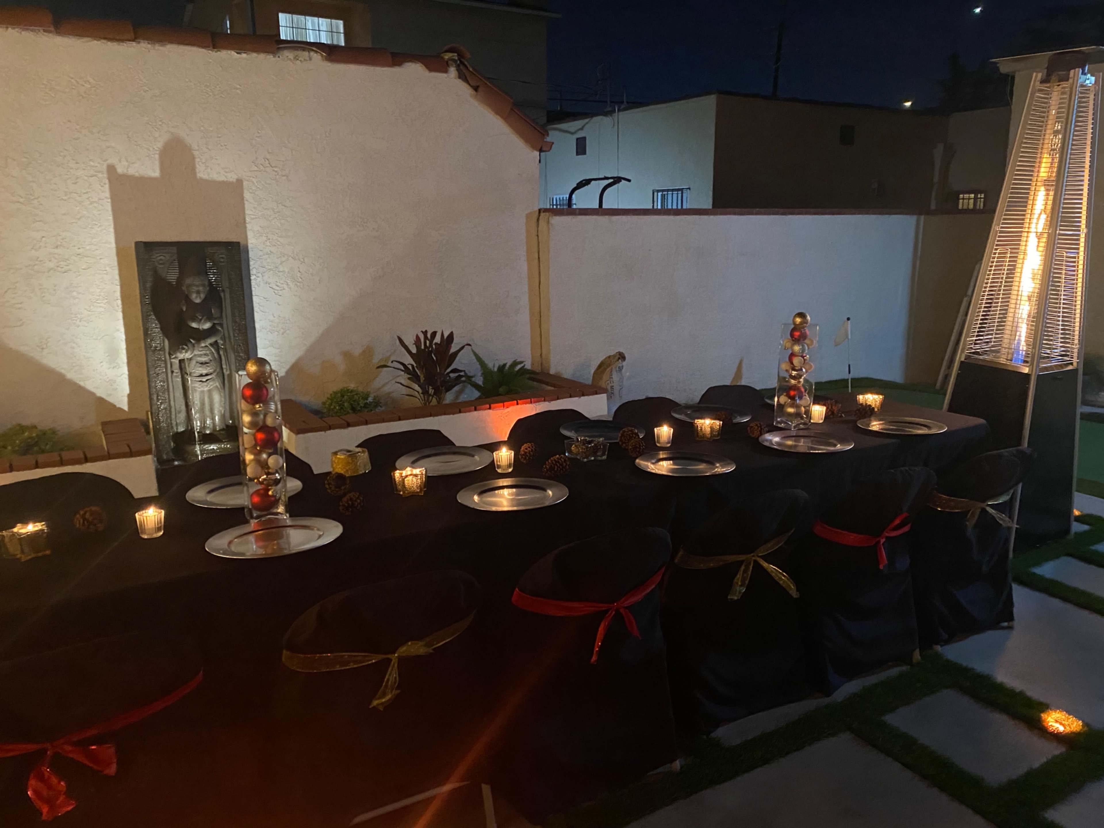 A long table is set for dining in an outdoor space, illuminated by candles and surrounded by decorative elements.