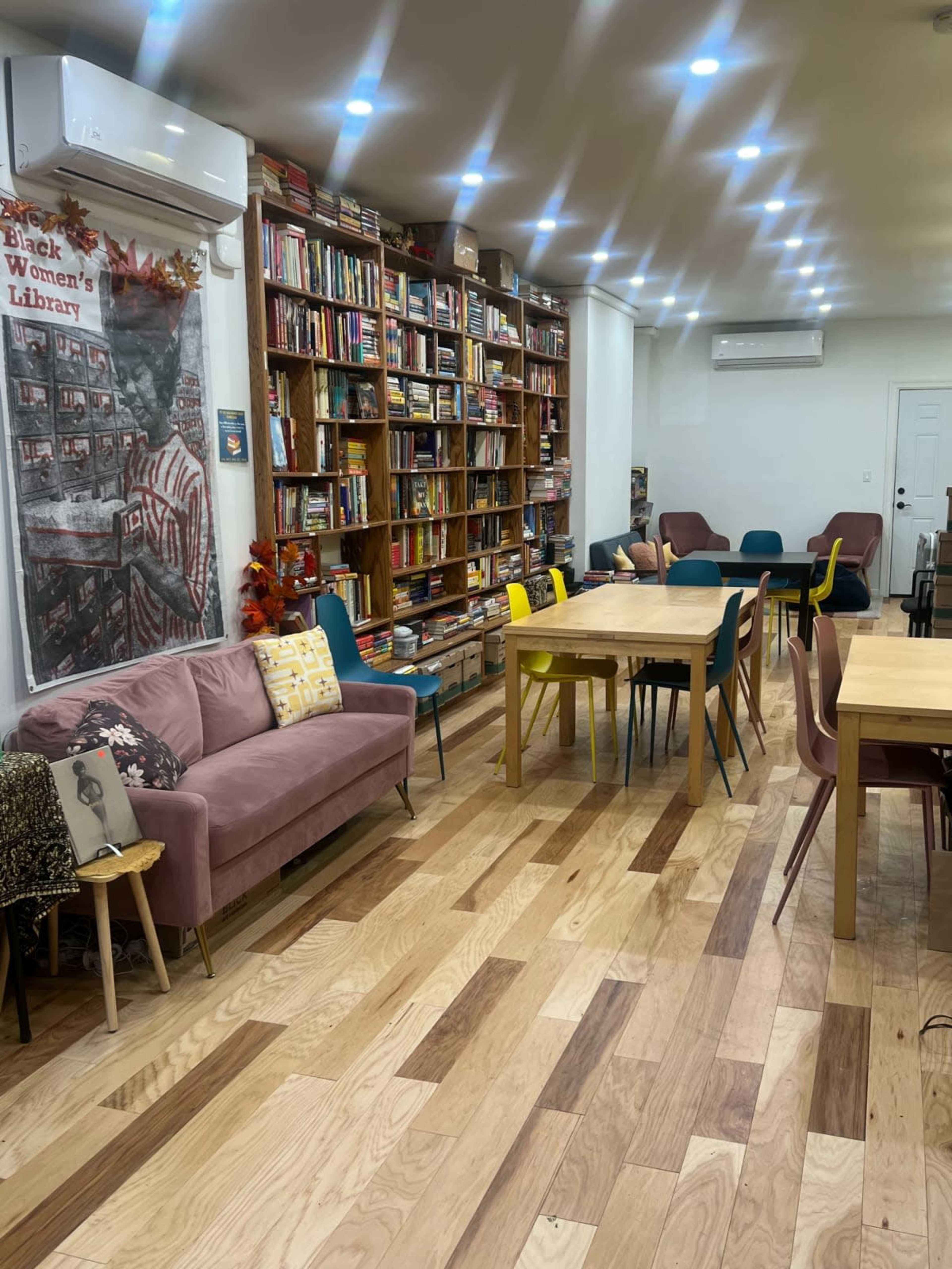 The room features a wall of bookshelves filled with books, a variety of seating including sofas and chairs, and wooden tables arranged on a wooden floor.
