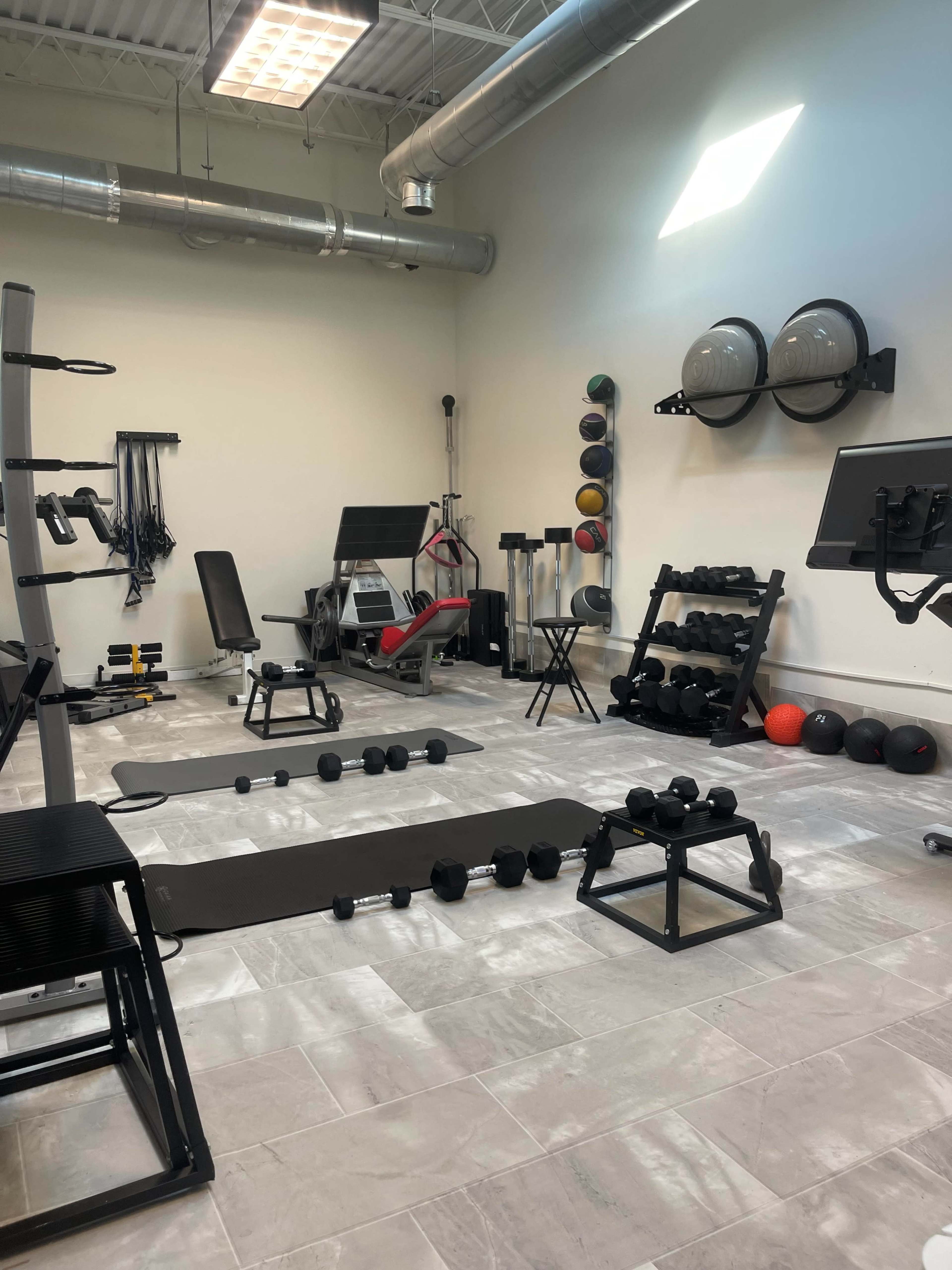 A well-equipped gym with various weights, exercise machines, and workout mats arranged in a spacious area.