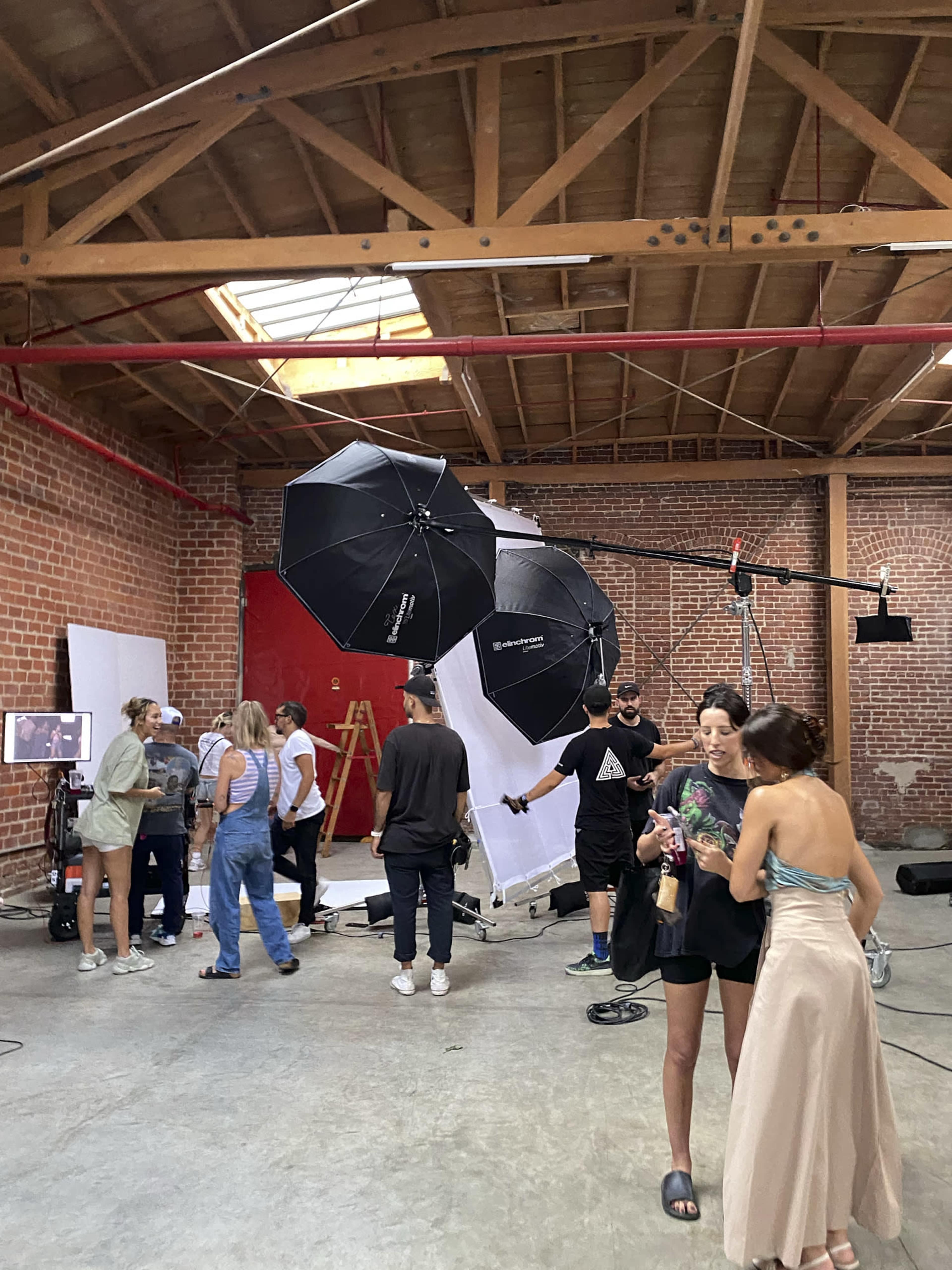 A group of people works on a photo shoot set in a studio with exposed brick walls and equipment like softboxes and a large backdrop.