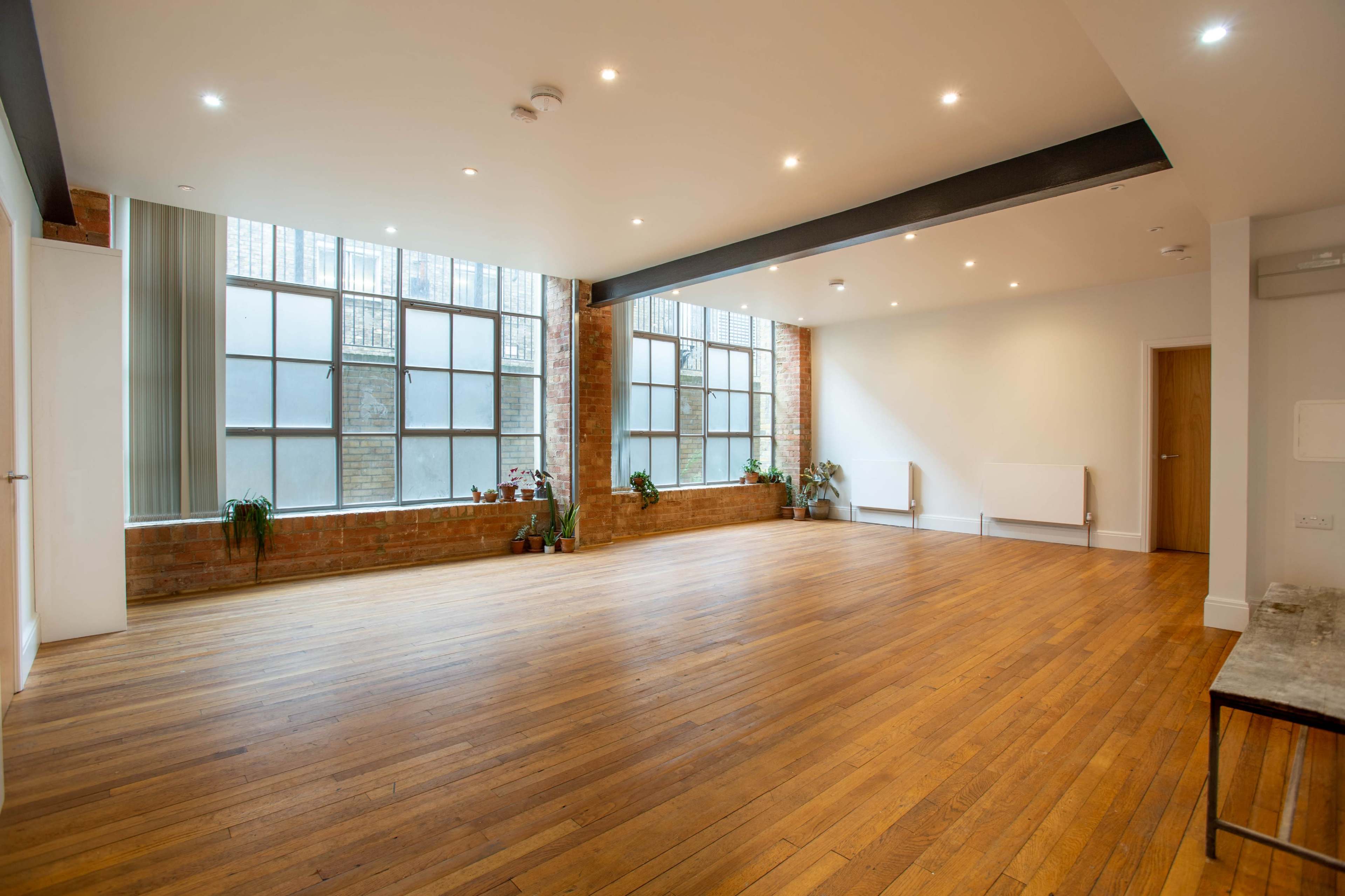A spacious room with large windows, brick walls, and wooden flooring.