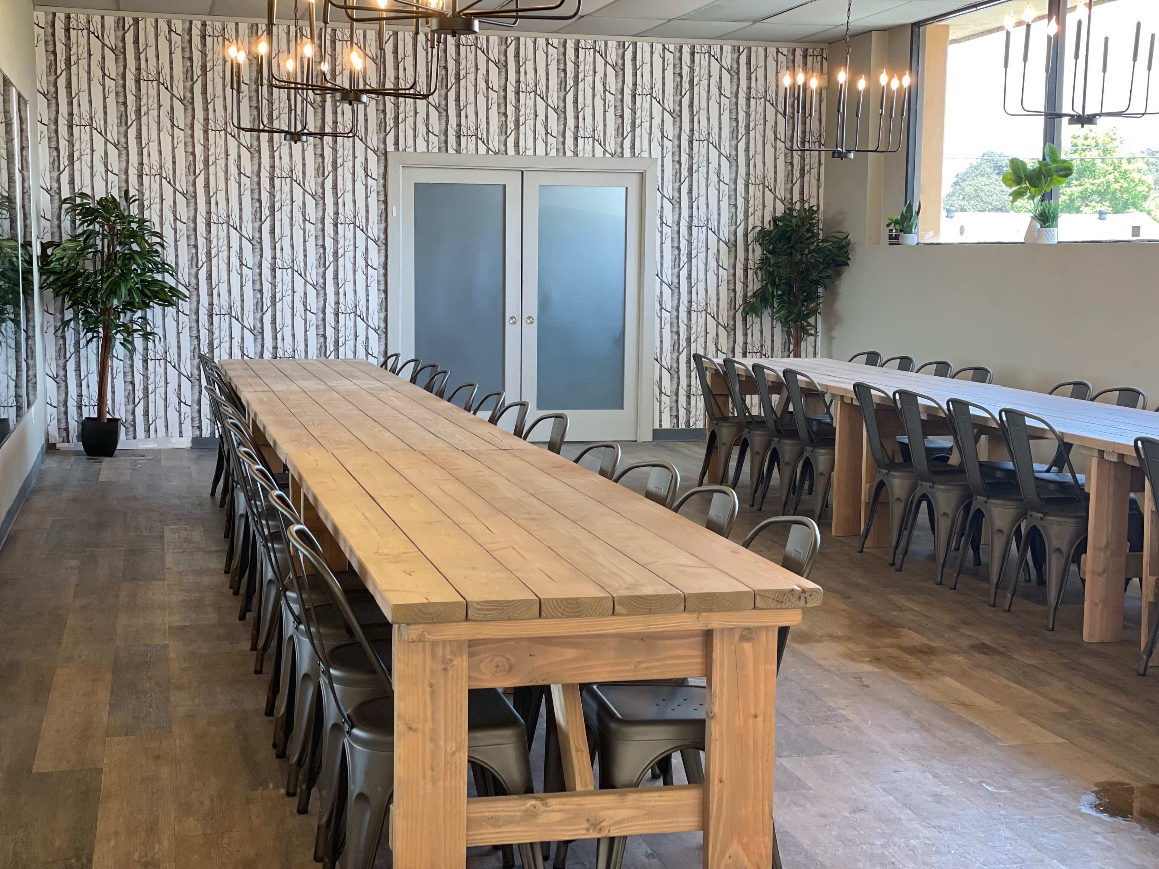 A spacious conference room with a long wooden table surrounded by metal chairs, decorated with a tree-patterned wall and large windows.