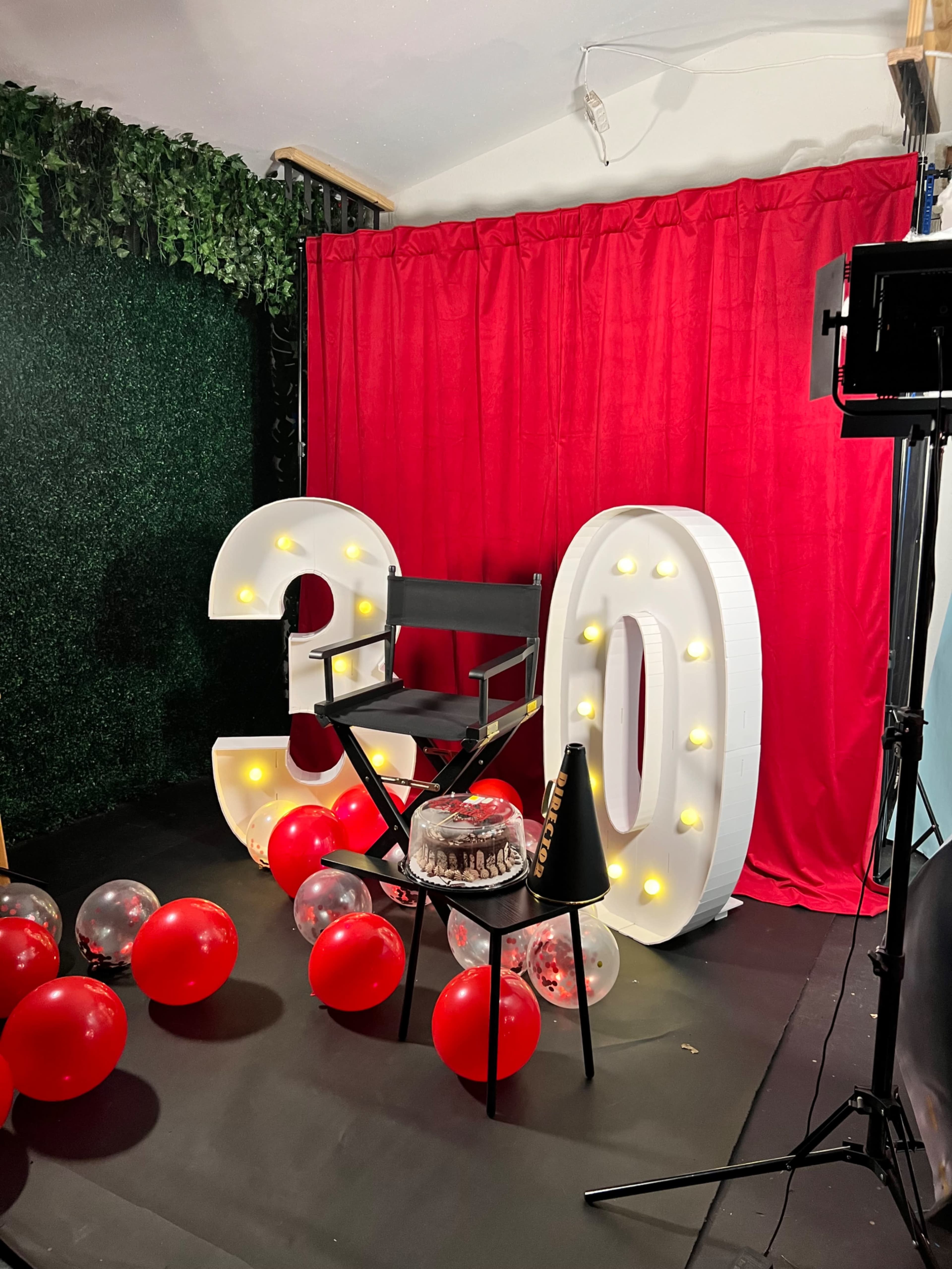 The scene features a decorated space with large illuminated numbers "30," a director's chair, and red and clear balloons on the floor.