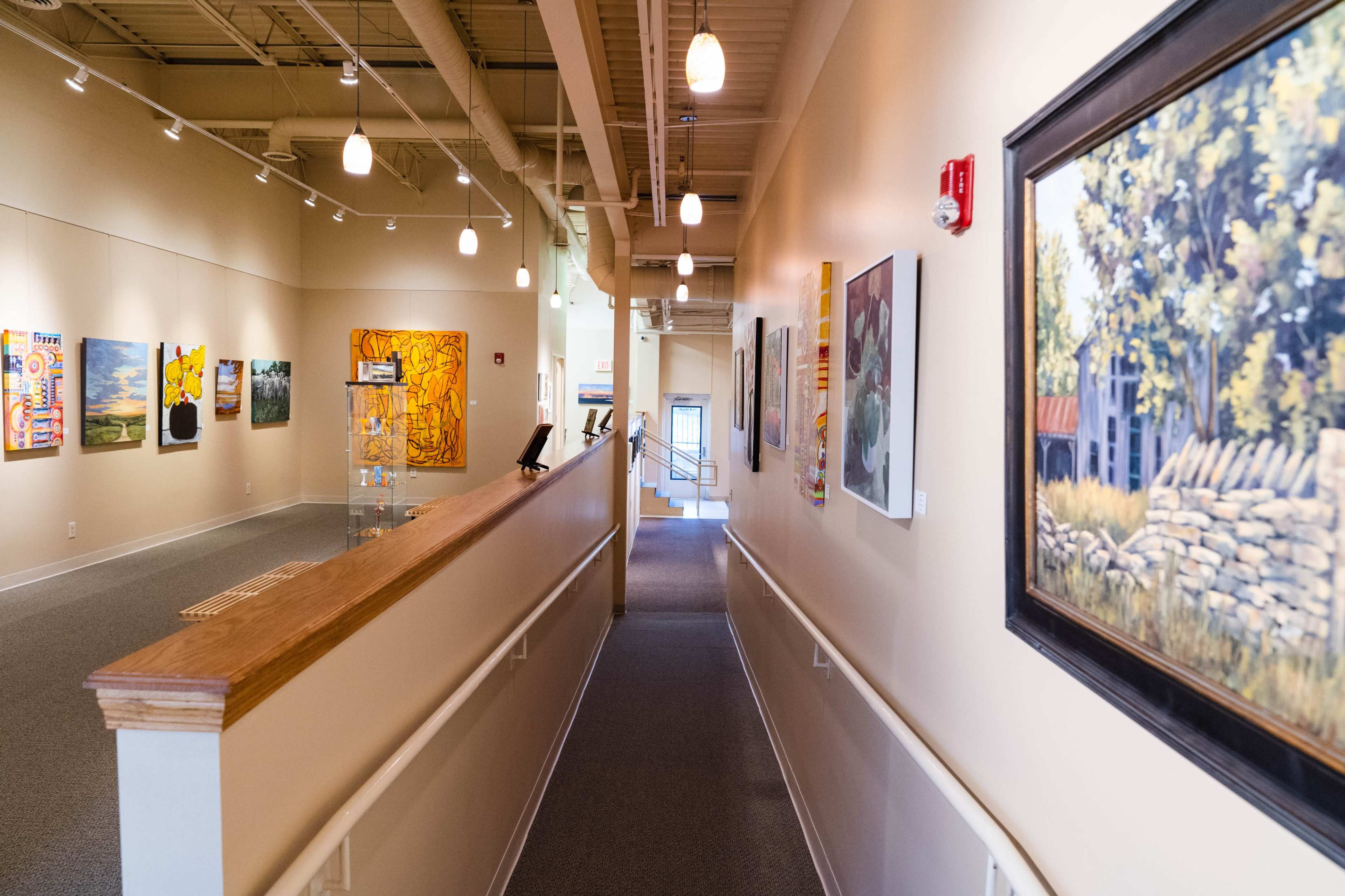 The scene shows a corridor in an art gallery with various paintings displayed on the walls and a railing along one side.