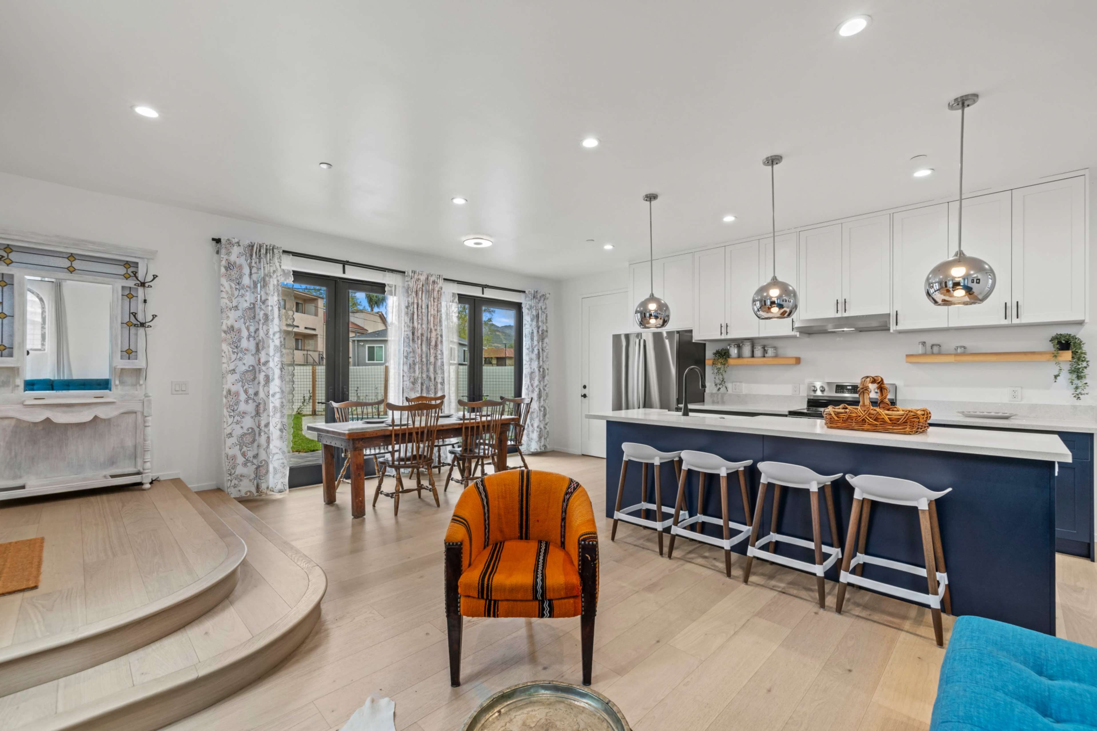 The image shows a modern kitchen and dining area featuring white cabinetry, a large island with seating, and a dining table with chairs near a window.