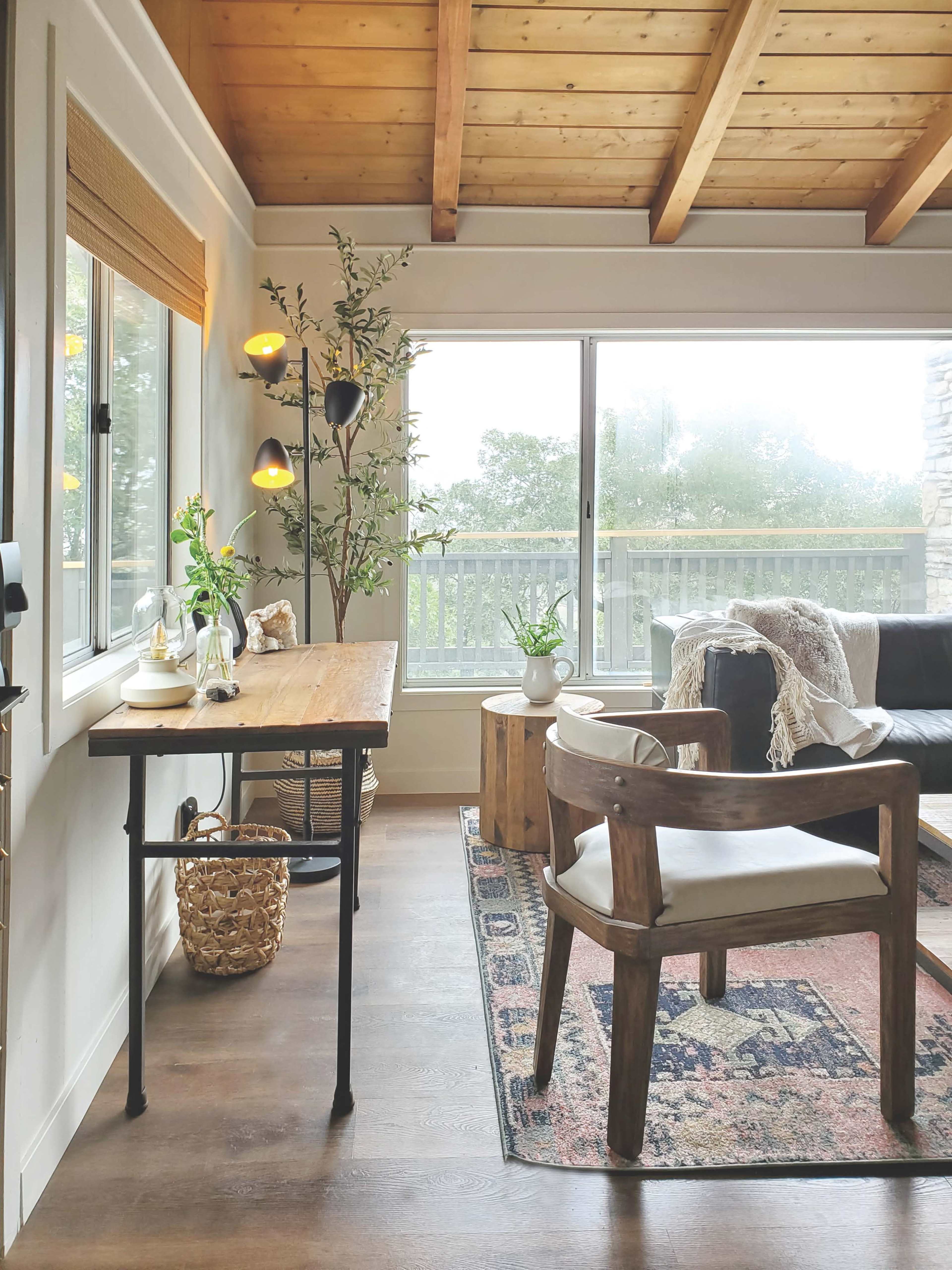 A cozy living space featuring a wooden desk, a brown chair, a potted plant, and a large window with natural light.