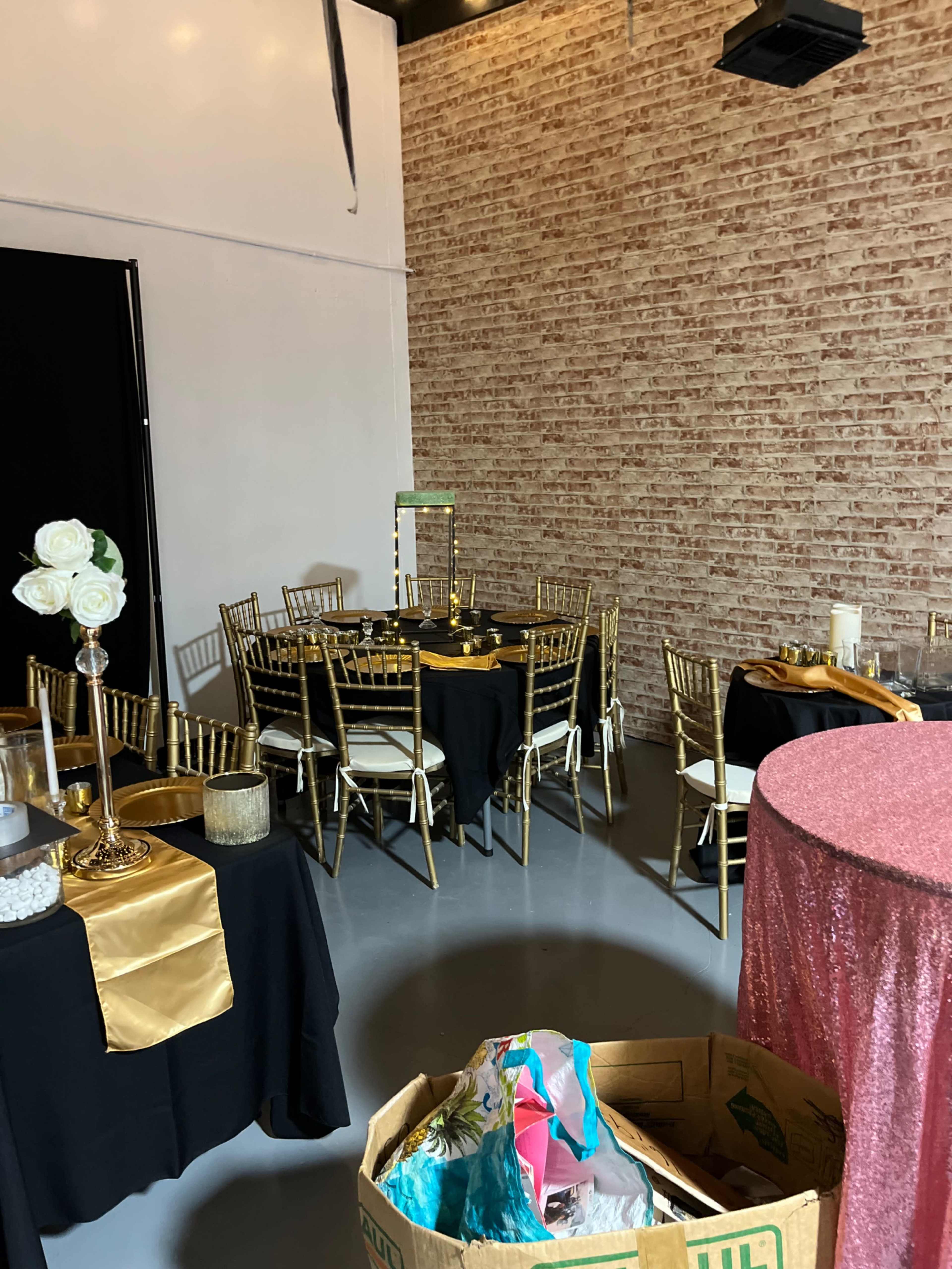 The scene shows a decorated event space with gold and black tables and chairs, set up for a gathering, alongside a box filled with miscellaneous items.