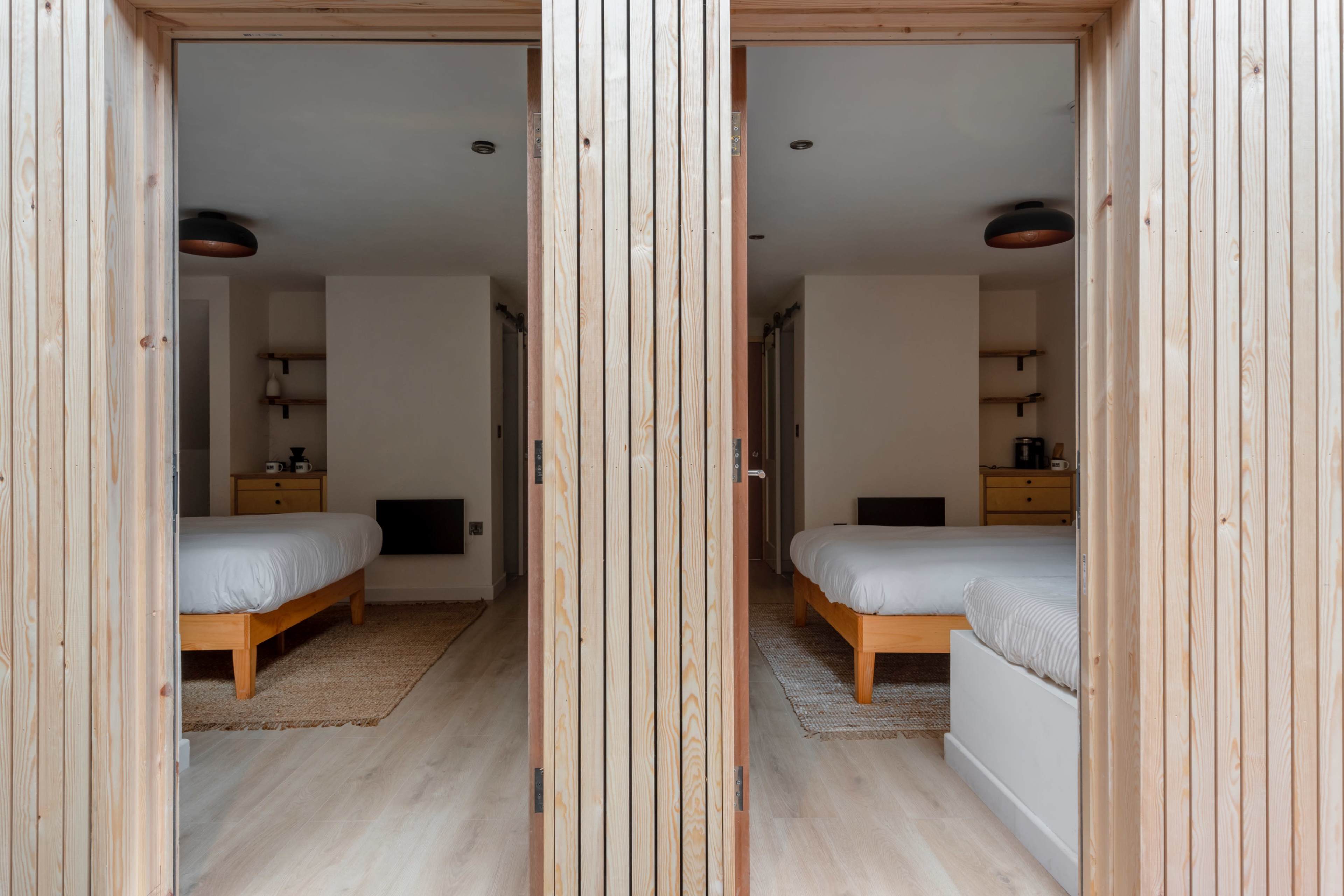 The image shows two identical bedrooms with wooden bed frames and simple decor, separated by a wooden doorframe.
