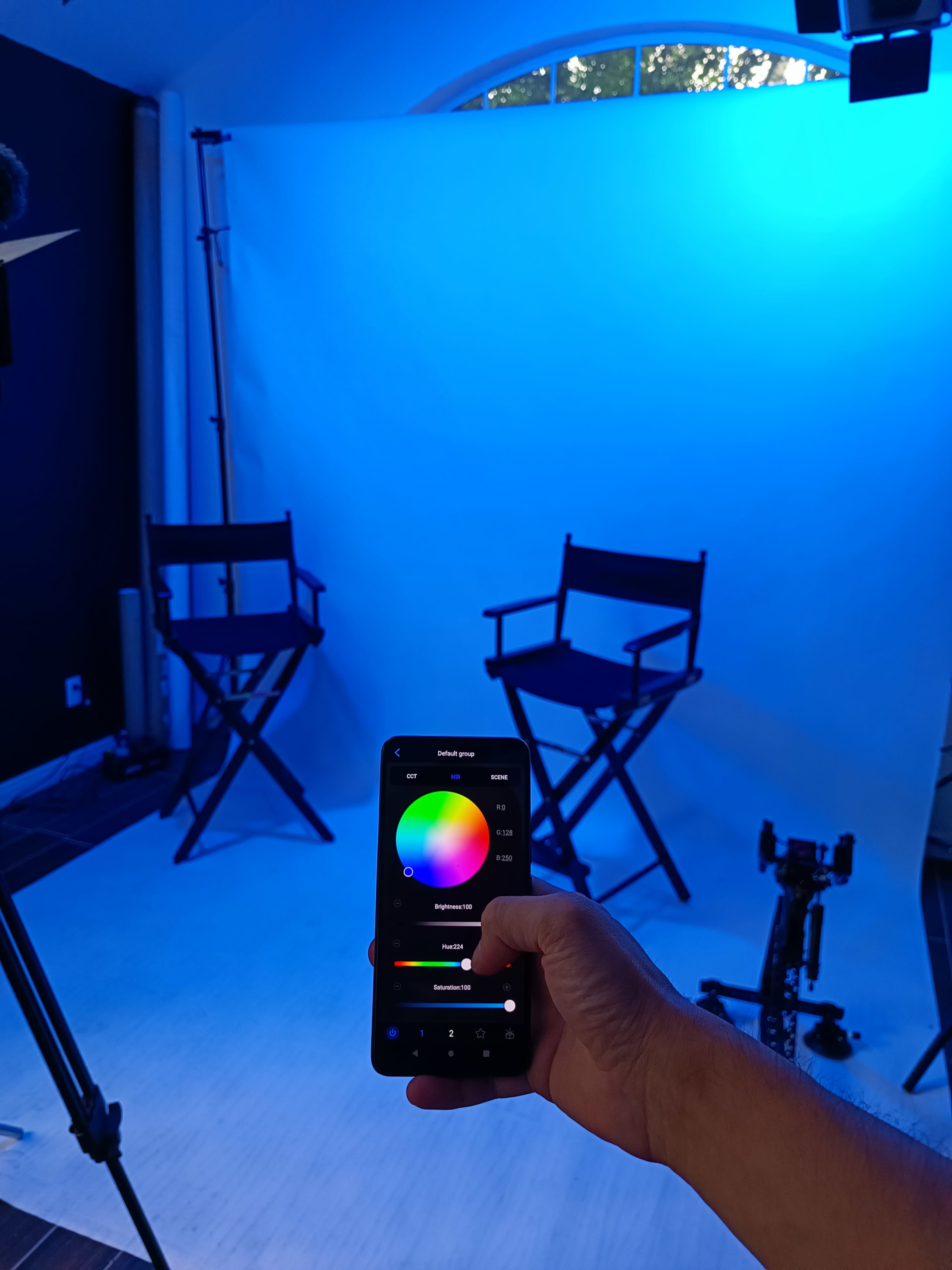 A person is holding a smartphone while configuring the lighting for a photography setup that includes two directors' chairs and a white backdrop.