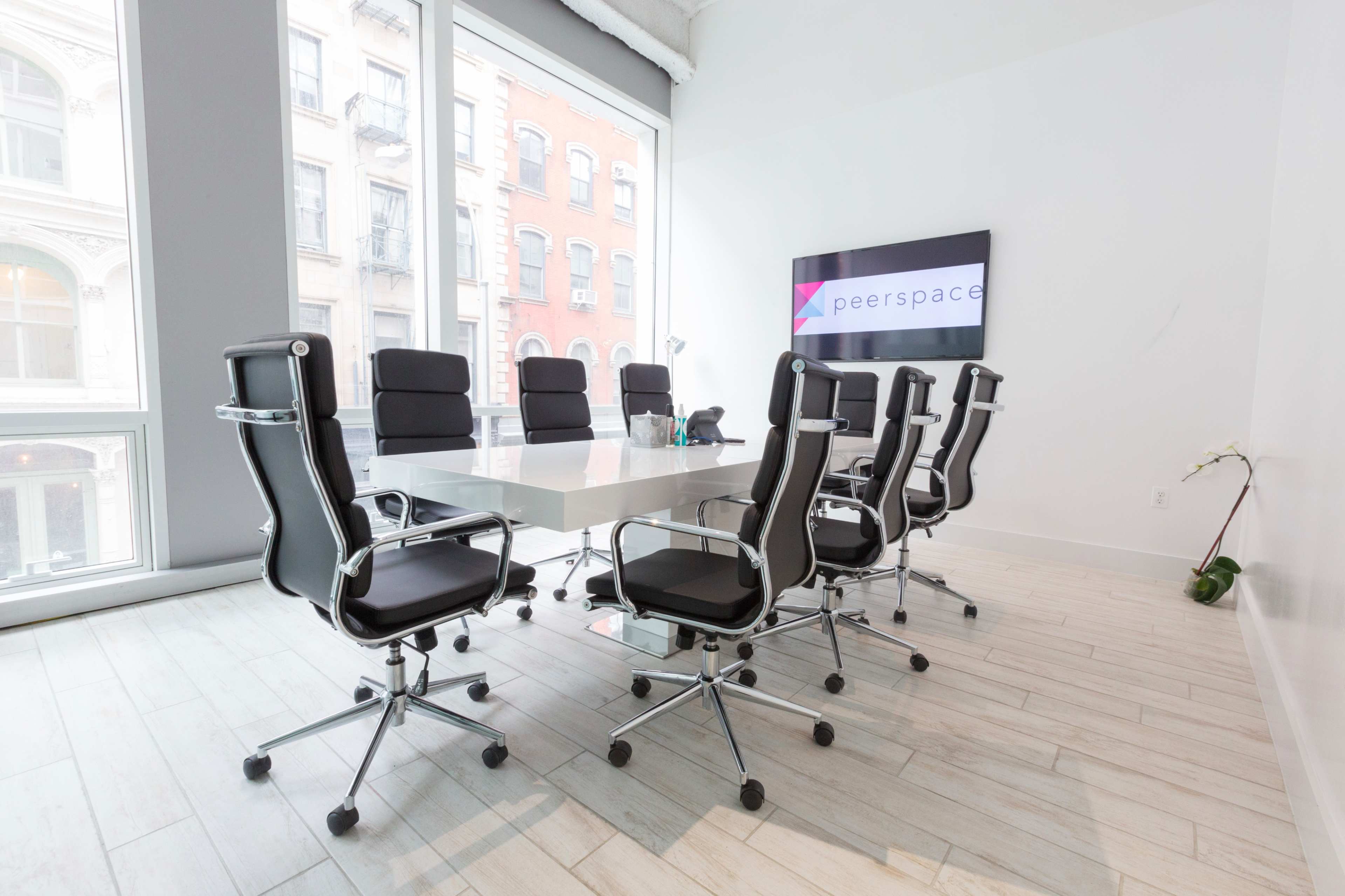 A modern conference room features a large white table surrounded by black swivel chairs, with a television displaying the Peerspace logo on the wall.