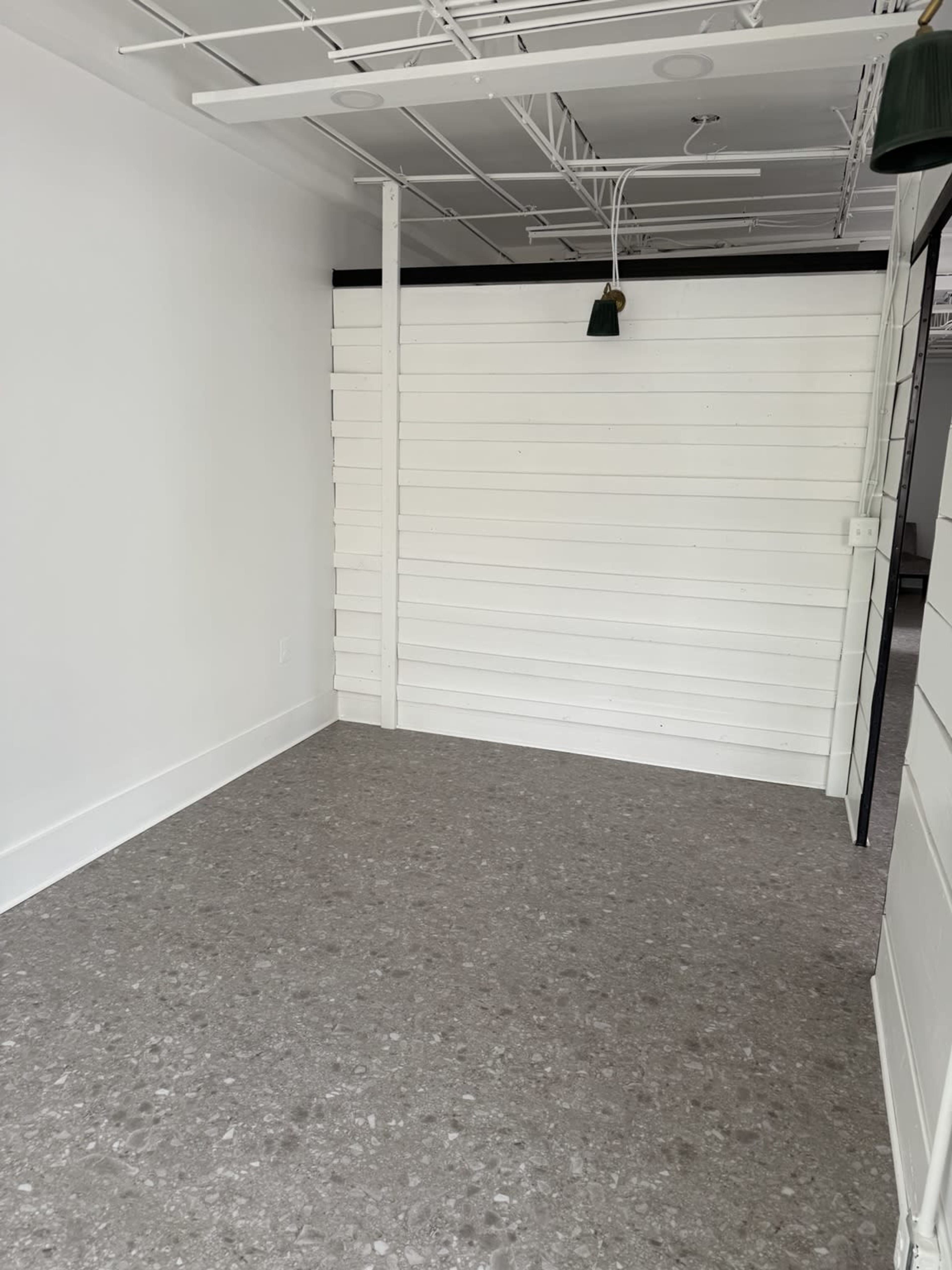 The image shows an empty room with white wooden walls and a gray, speckled floor.