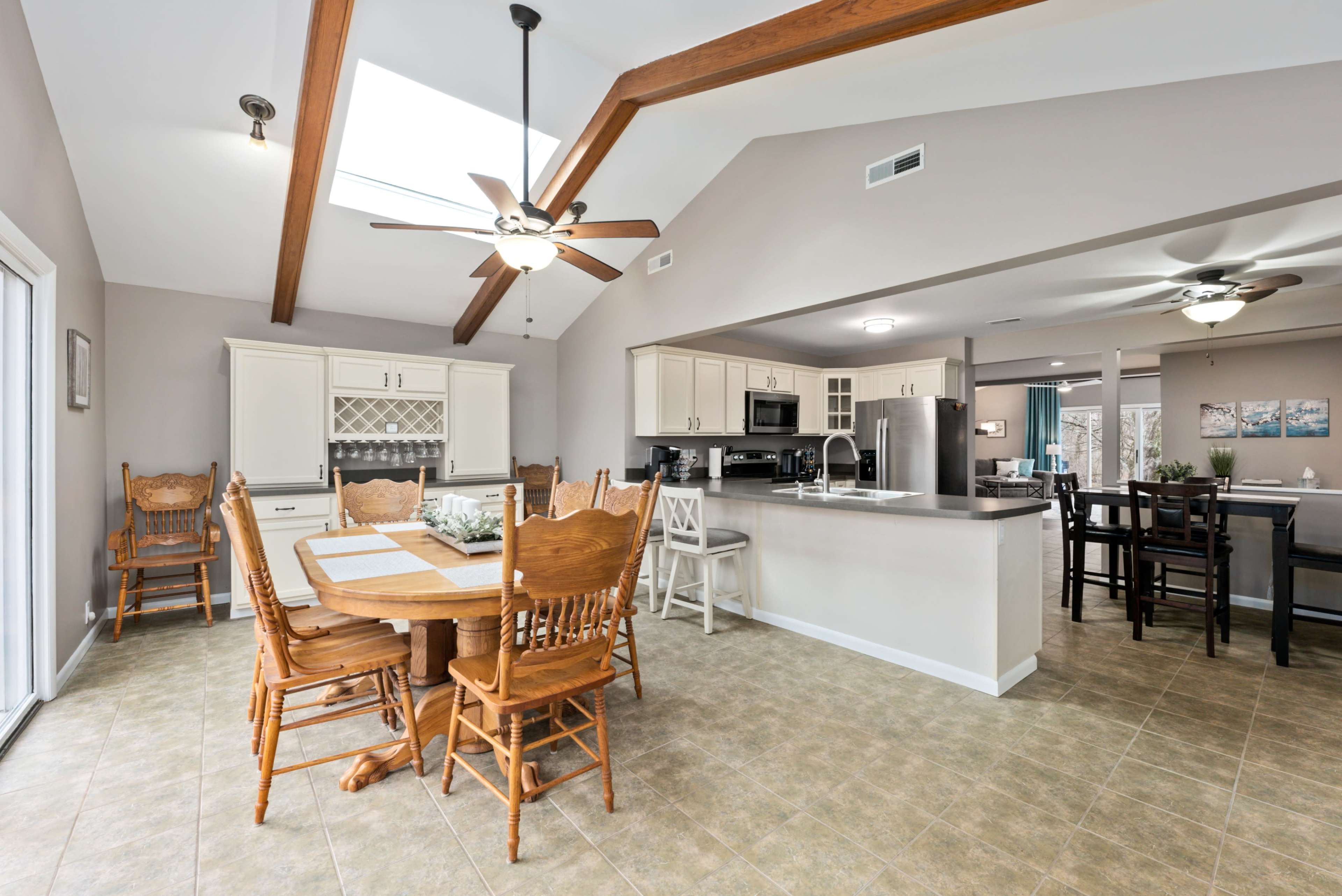 A spacious kitchen and dining area features a wooden table surrounded by chairs, with a ceiling showcasing exposed beams and skylights.