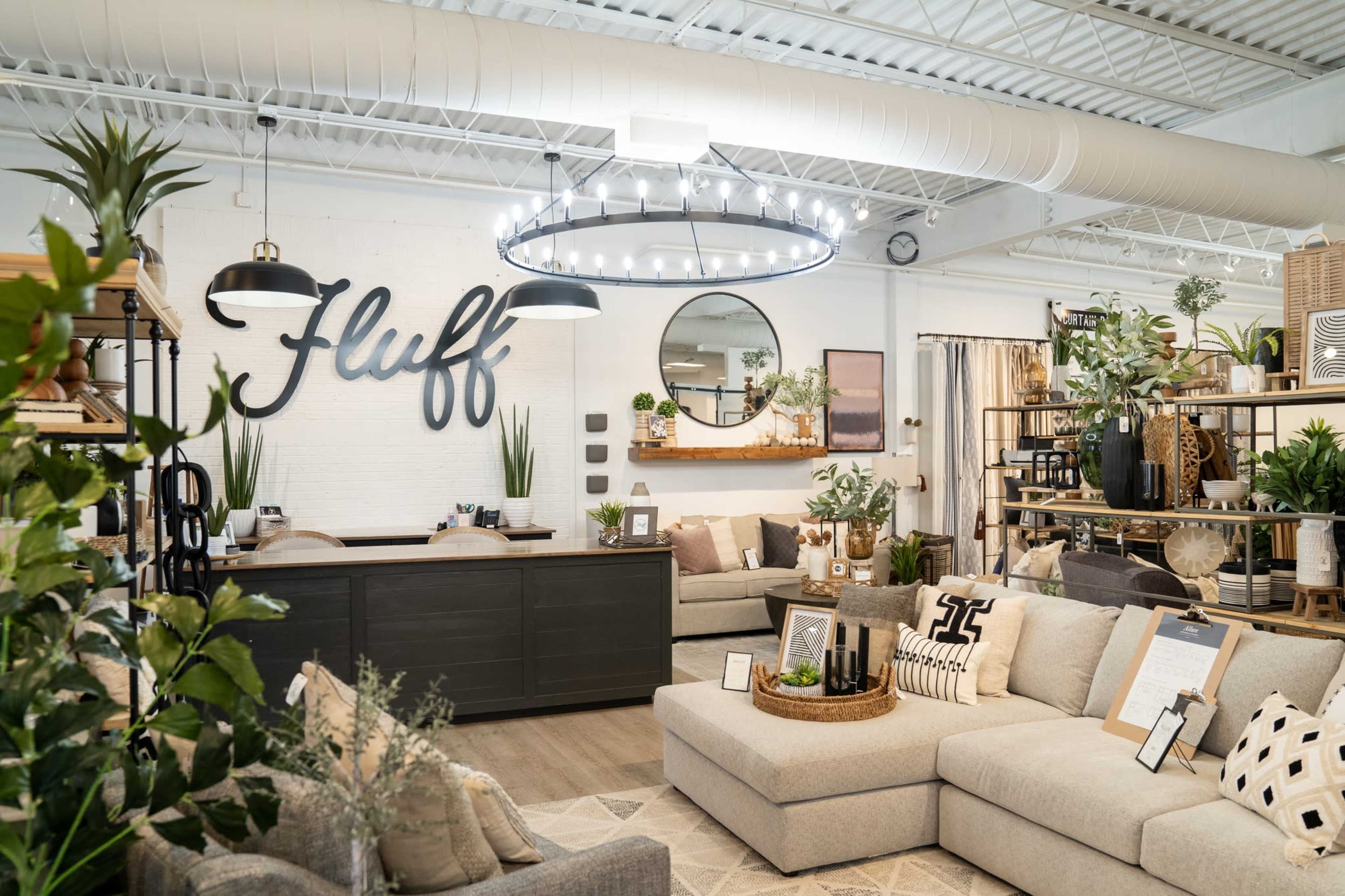 The image shows a modern home decor showroom featuring a reception desk, various sofas, and decorative plants arranged on shelves.