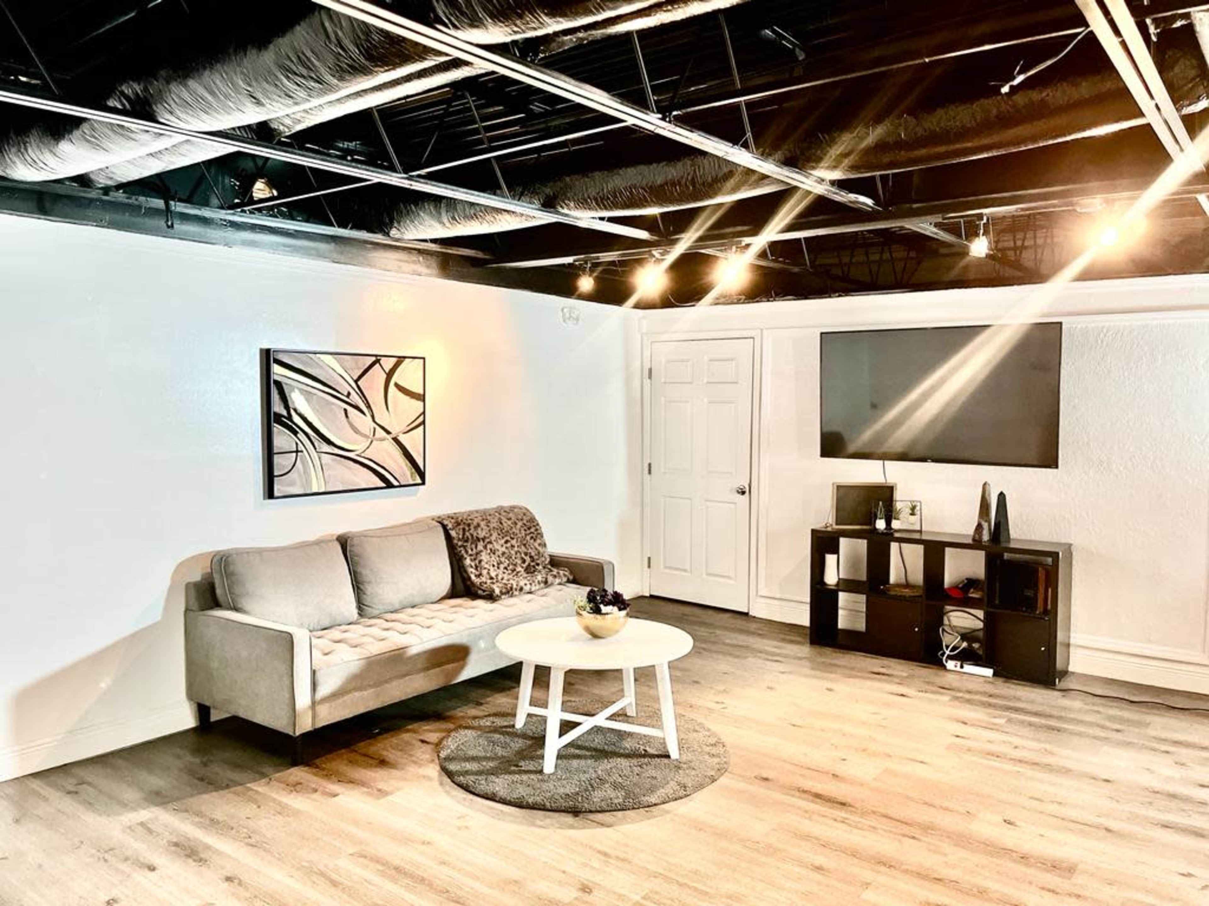 A modern, minimalistic living space with a gray sofa, a round coffee table, and a television mounted on the wall.