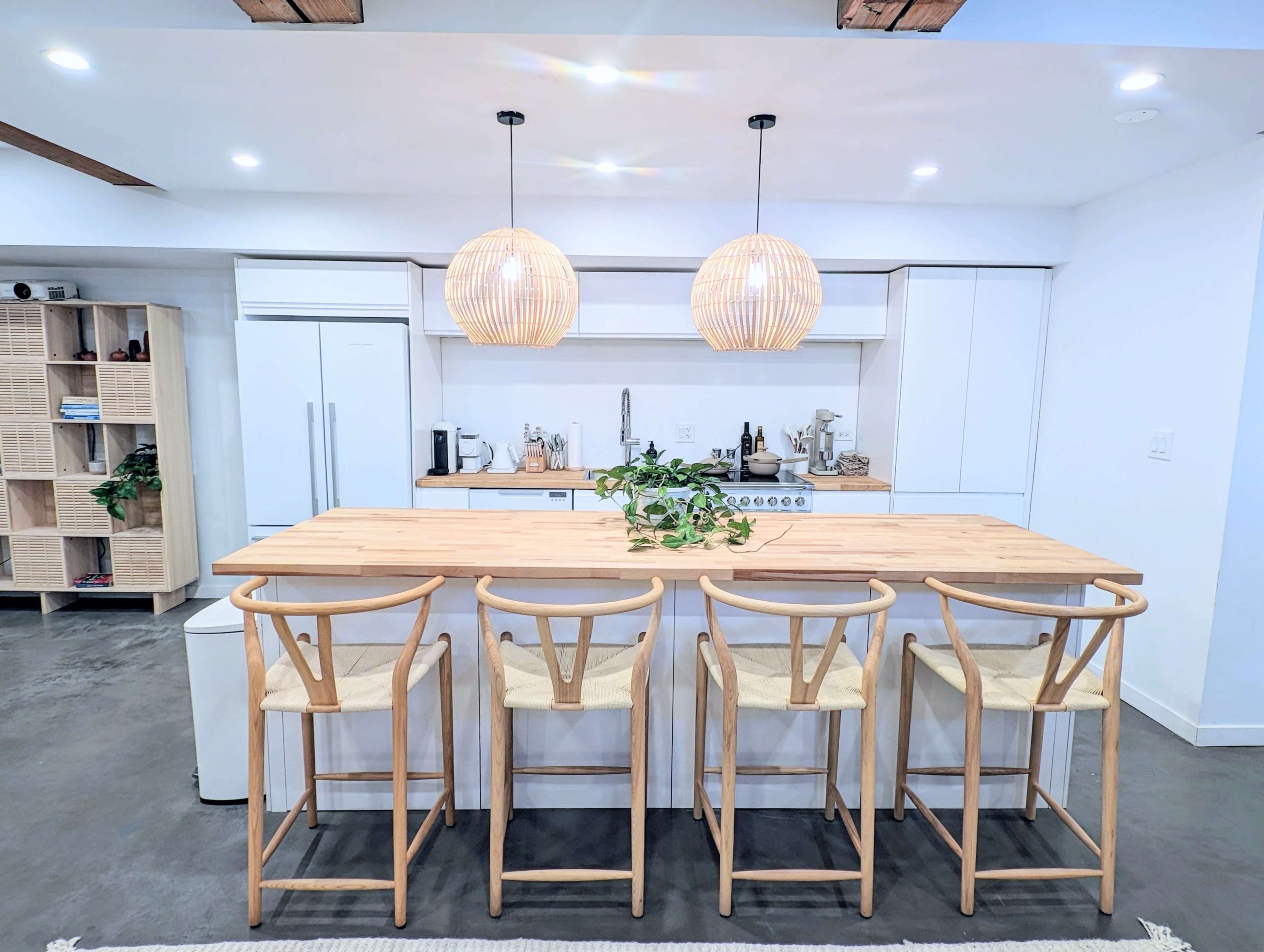 A modern kitchen features a wooden dining table with five high stools and two pendant lights overhead.