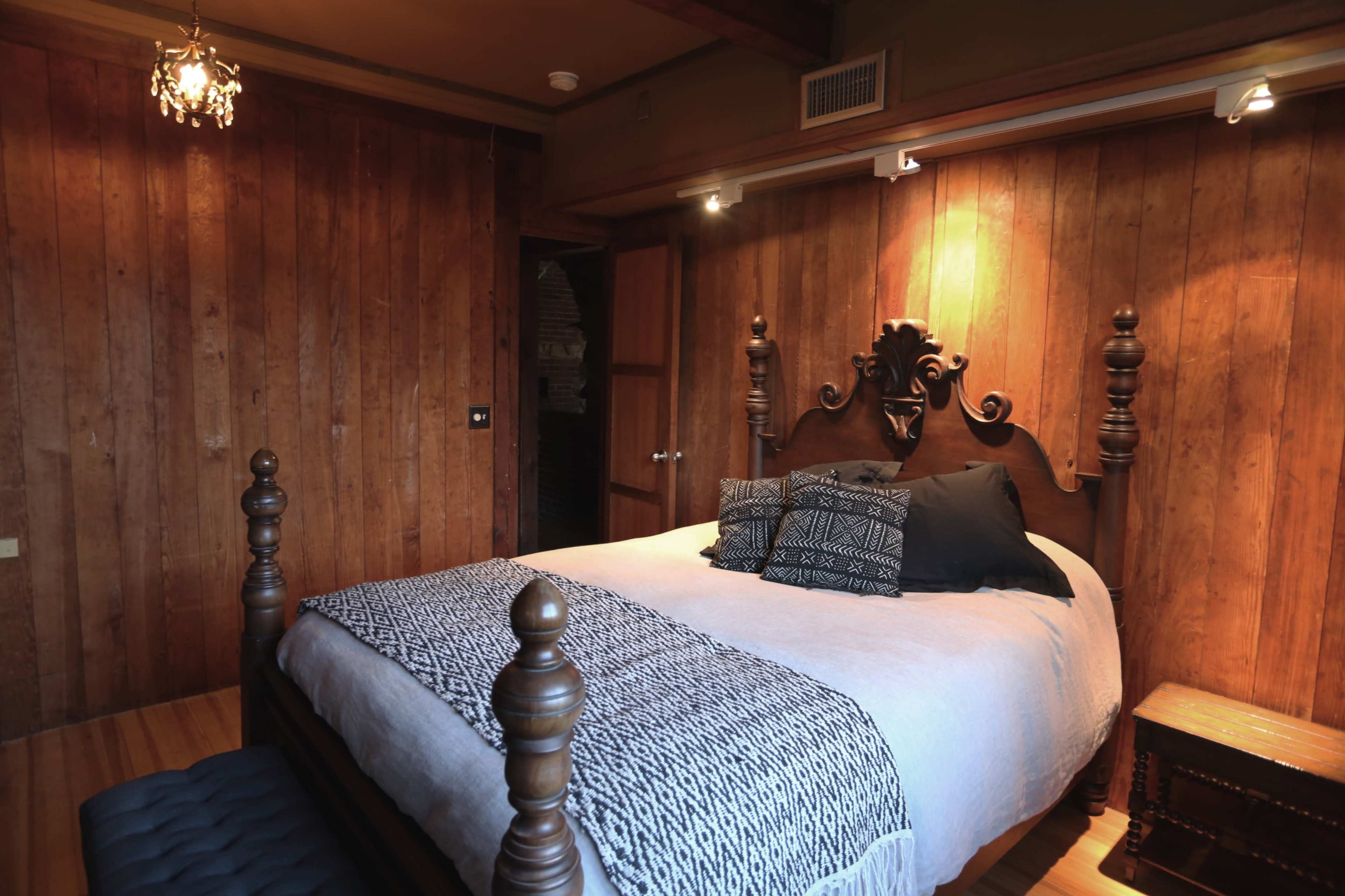 A bedroom with wooden walls, a large bed with a decorative headboard, and a patterned throw blanket.