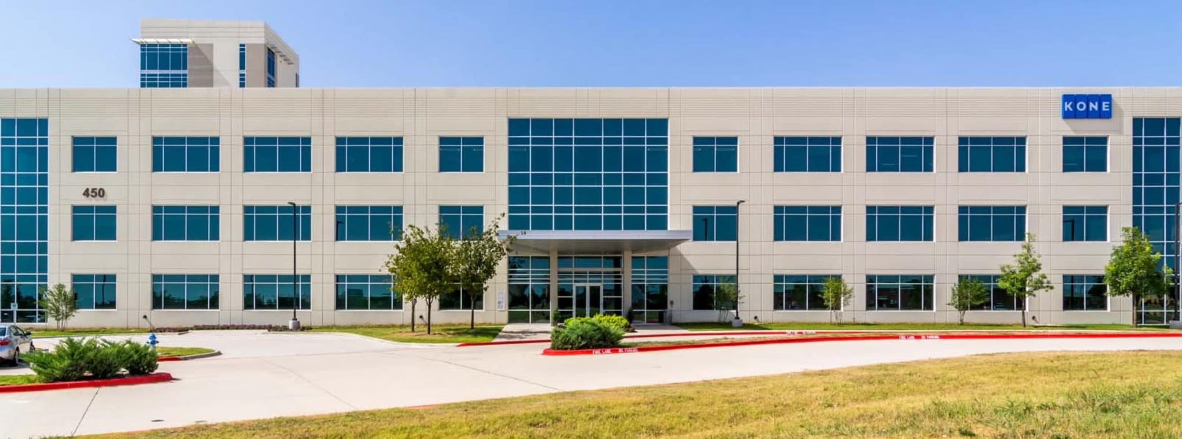 The image shows a modern, multi-story office building with large glass windows and a sign that reads "KONE" on the upper-right side.