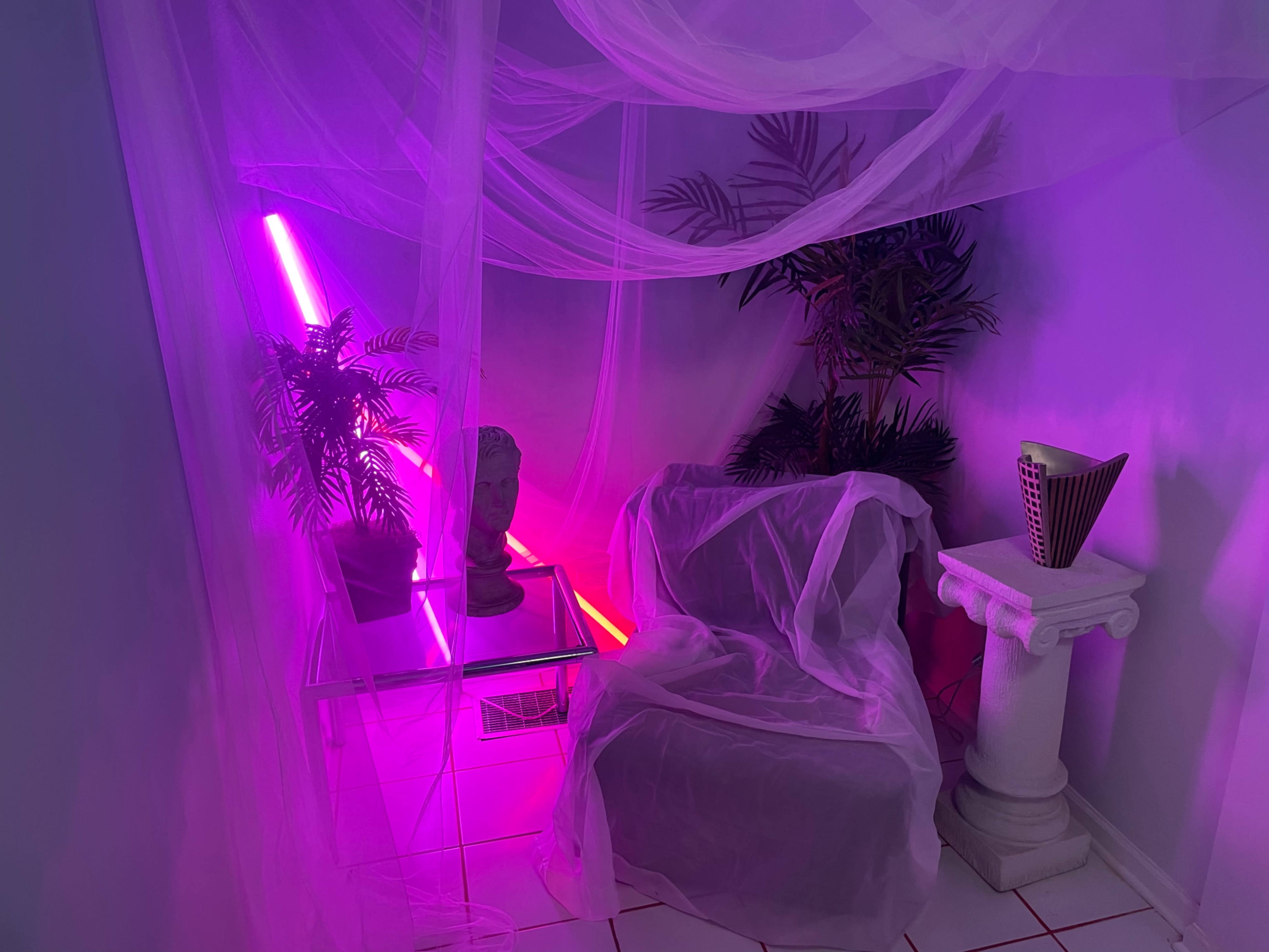 The scene features a small corner with a sofa draped in sheer fabric, illuminated by pink and purple neon lights, alongside potted plants and a decorative pedestal with a bust.