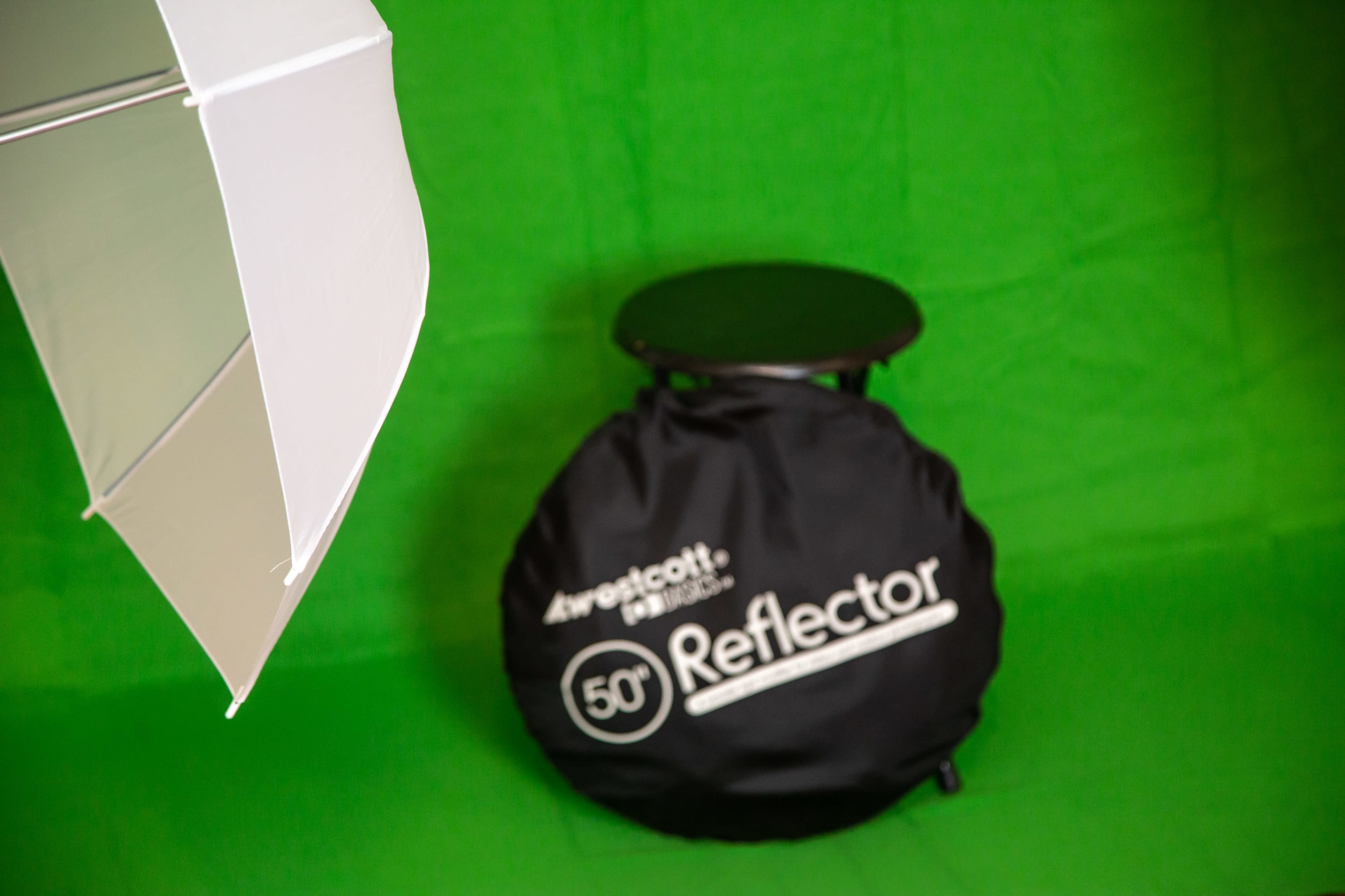 A black folding stool and a white umbrella reflector set against a green backdrop.