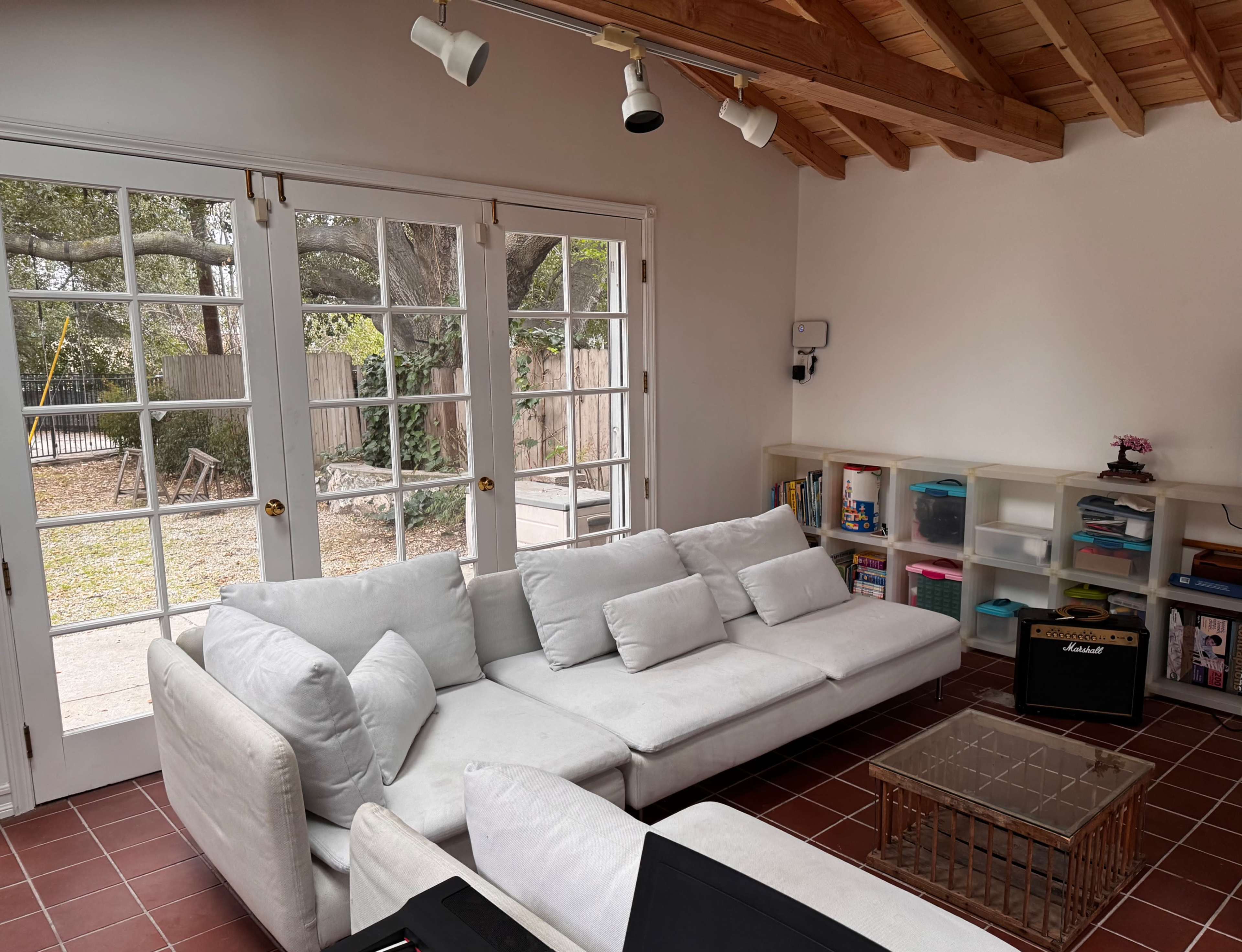 A modern living room features a white sectional sofa and a glass coffee table, with large French doors leading to a patio.