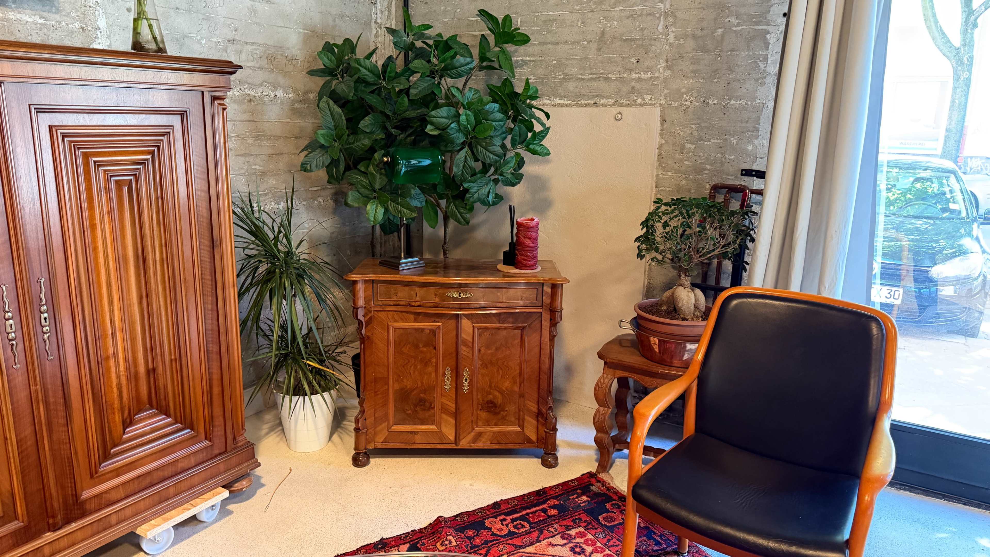 The image shows a corner of a room featuring wooden furniture, a potted plant, and a black chair with a wooden frame.
