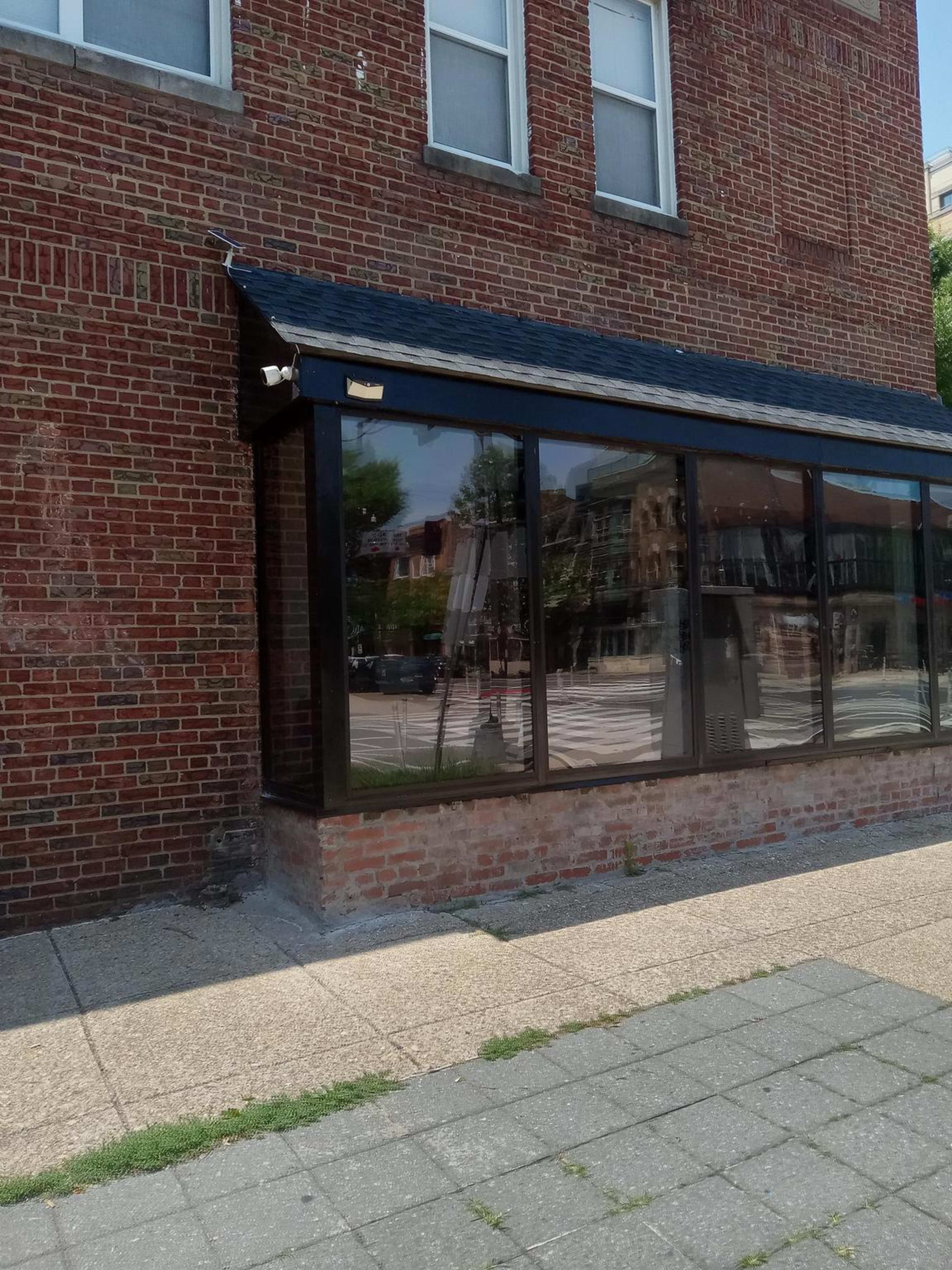 The image shows the corner of a brick building with a glass storefront and a paved sidewalk in front.