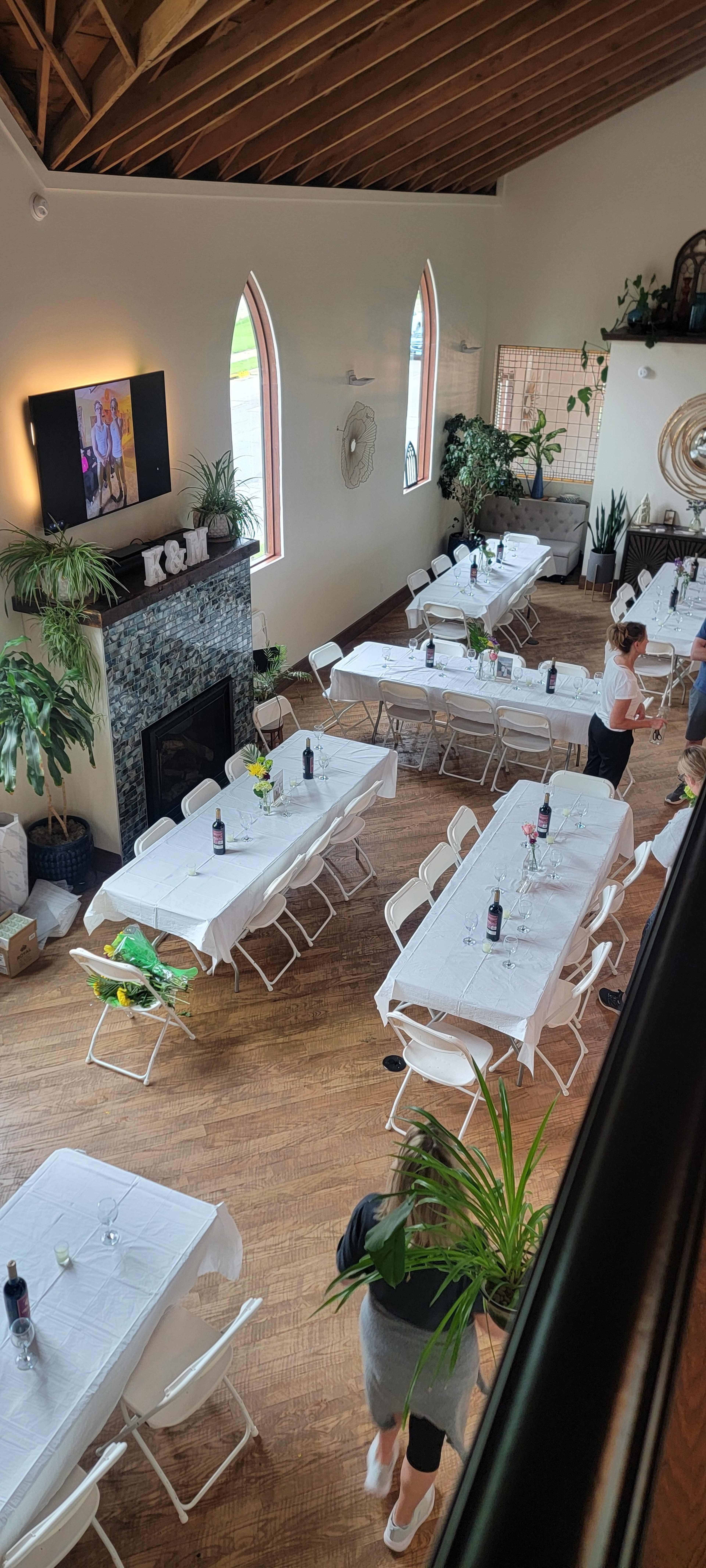 The image shows a spacious, well-lit dining area with rows of neatly arranged tables covered with white tablecloths and a large television mounted on the wall.