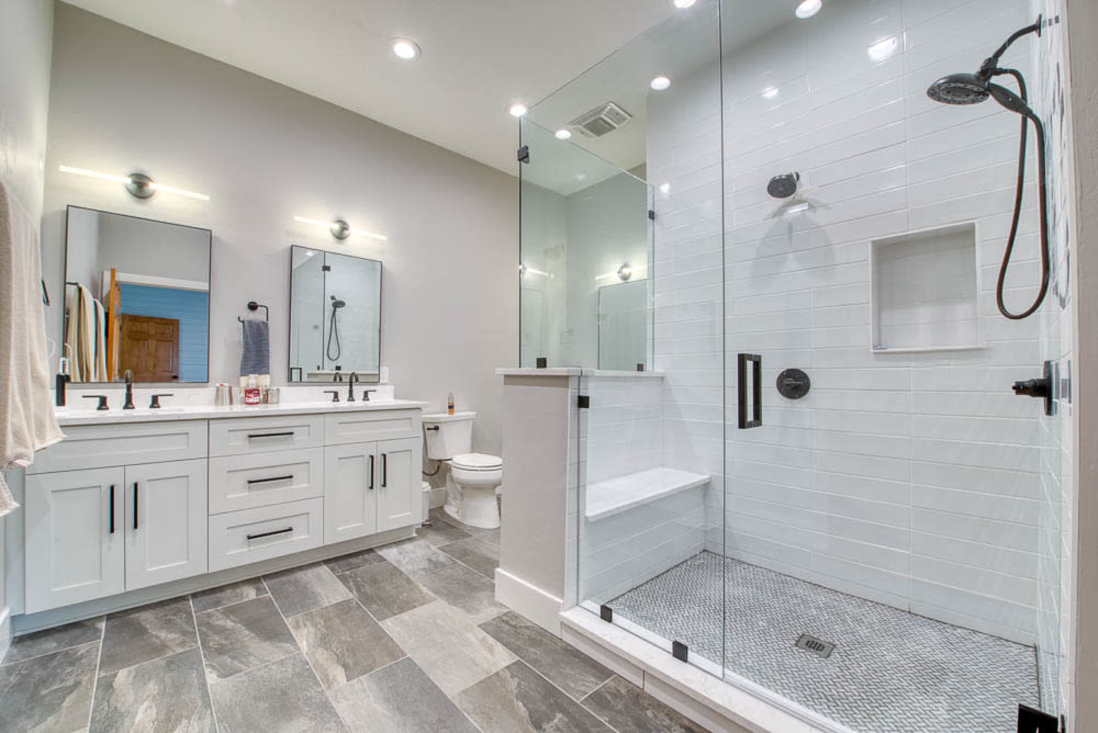 A modern bathroom features a glass shower enclosure, double vanity with sinks, and neutral-colored tiles.