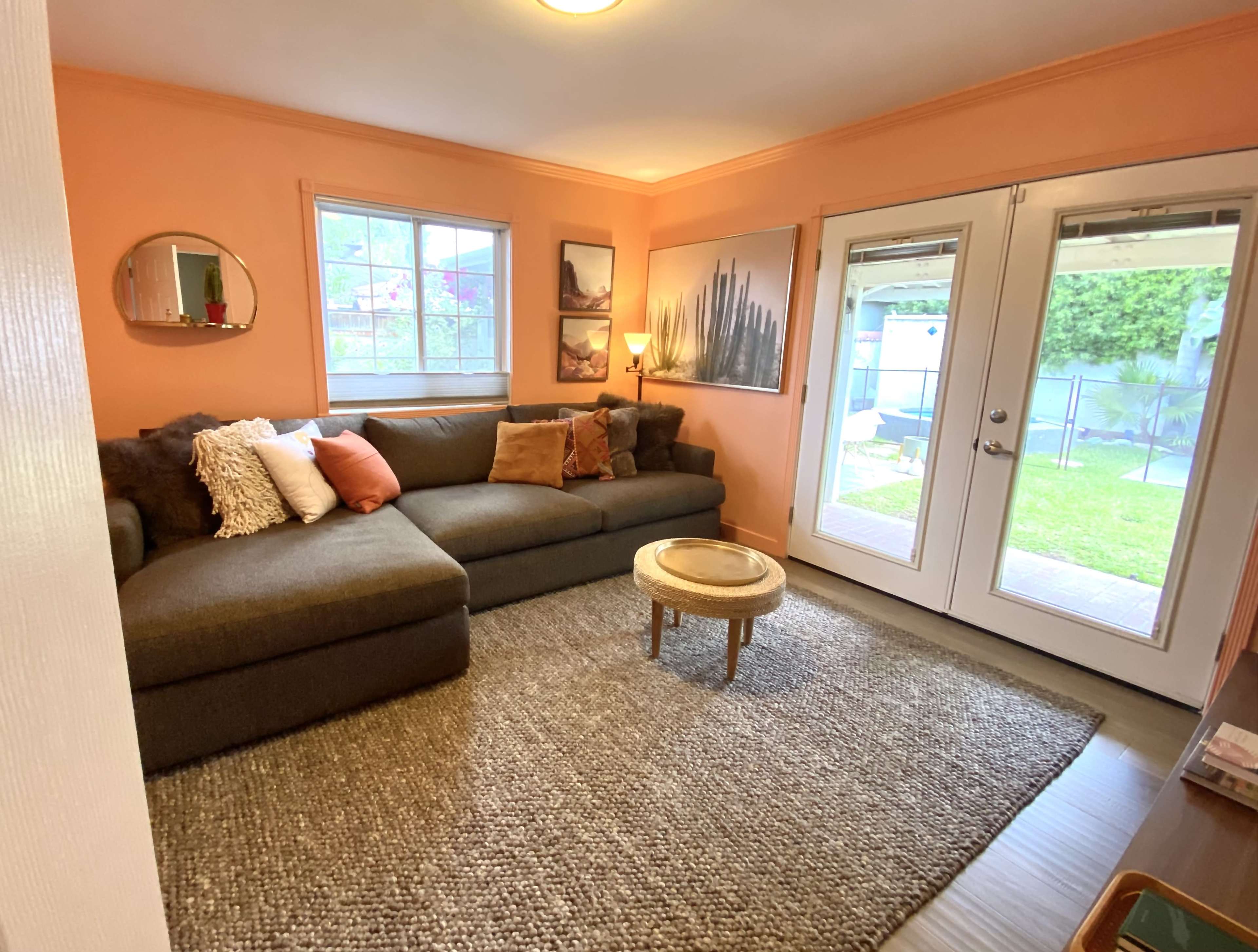 A cozy living room featuring a large sectional sofa, a round coffee table, and two glass doors leading to an outdoor area, all set against a light orange wall.