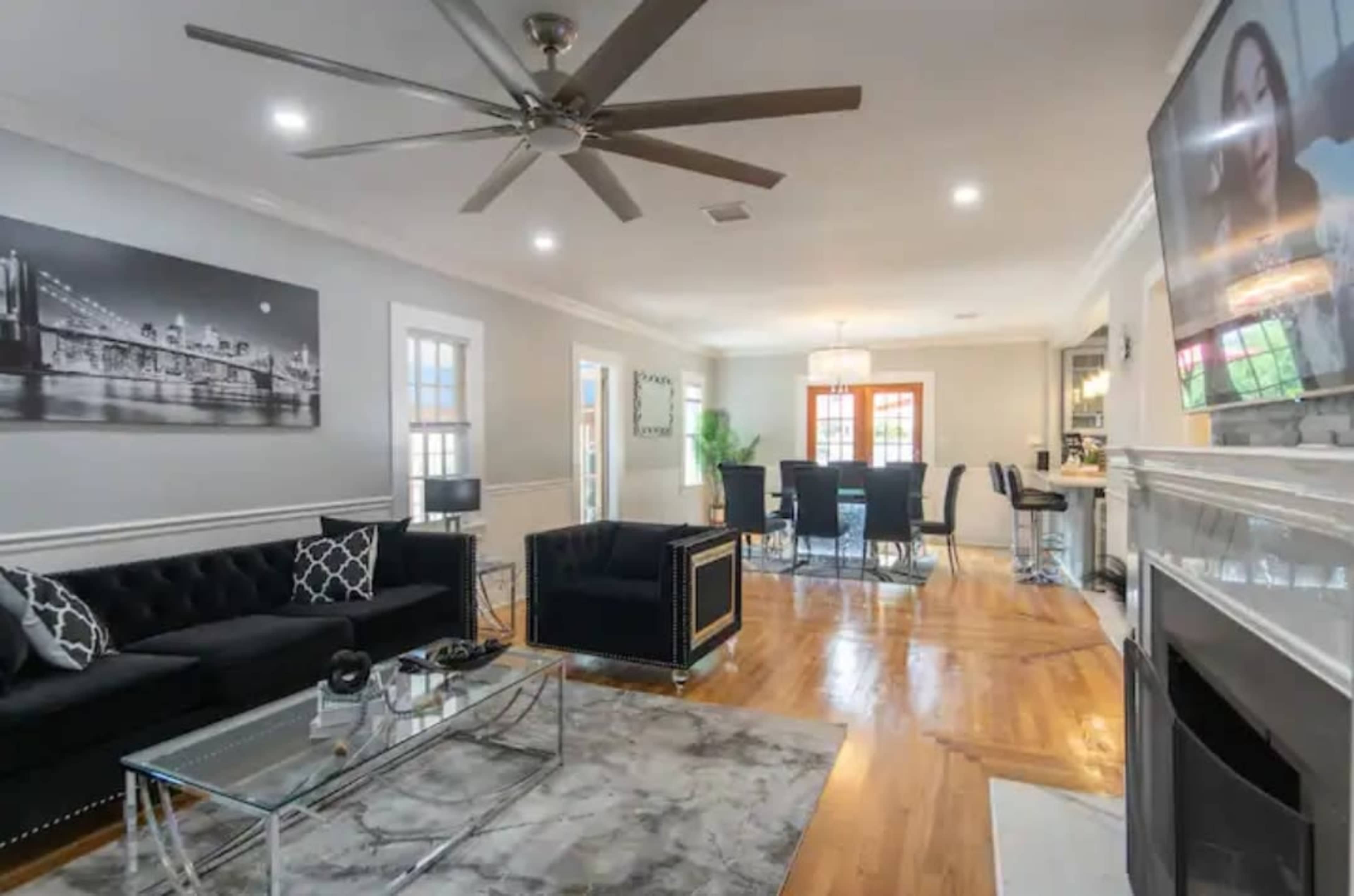 The room features a modern living area with a black sofa, a glass coffee table, and a dining area in the background.