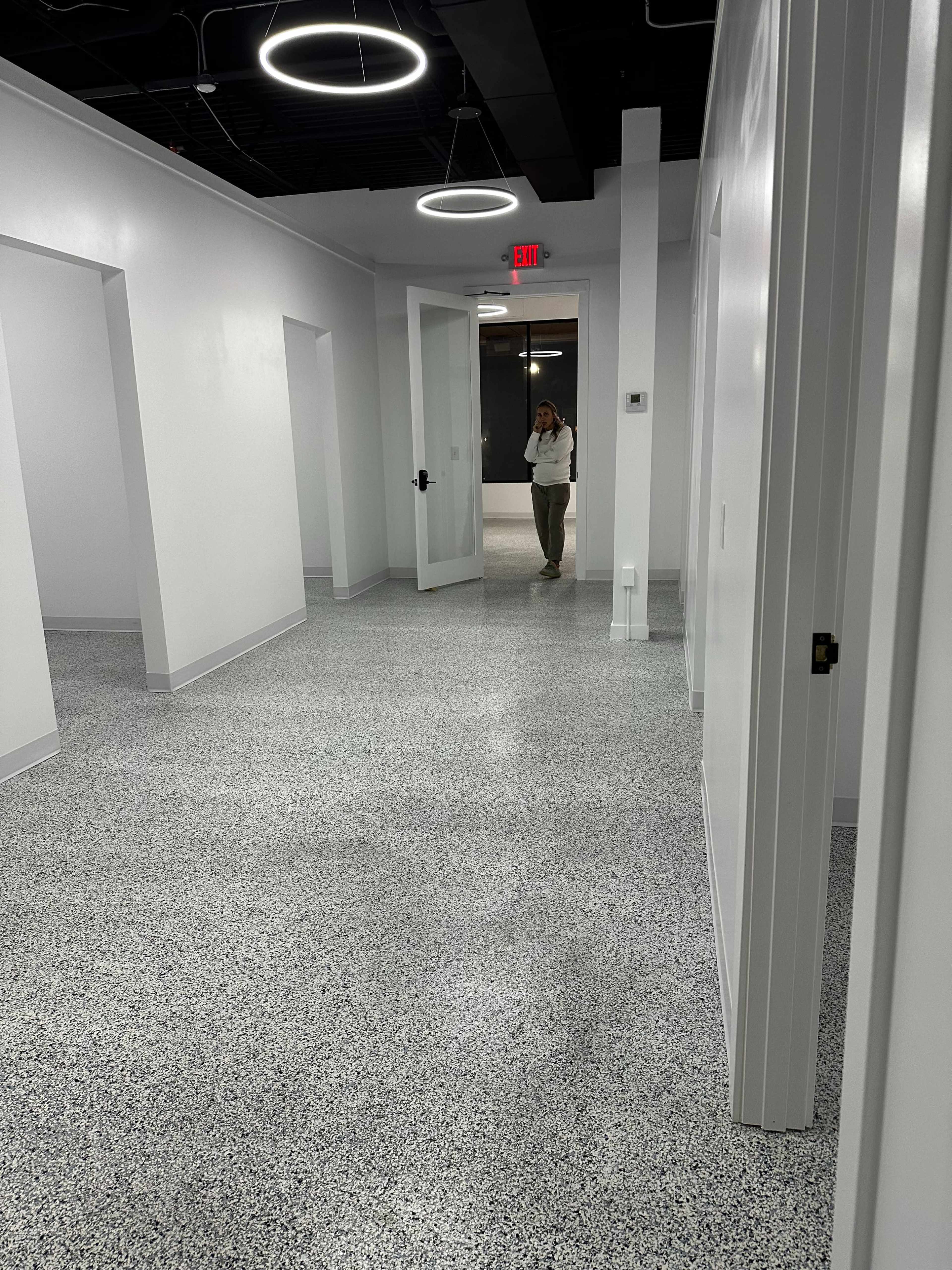 A woman stands in a modern hallway with white walls and a speckled floor, framed by circular light fixtures.