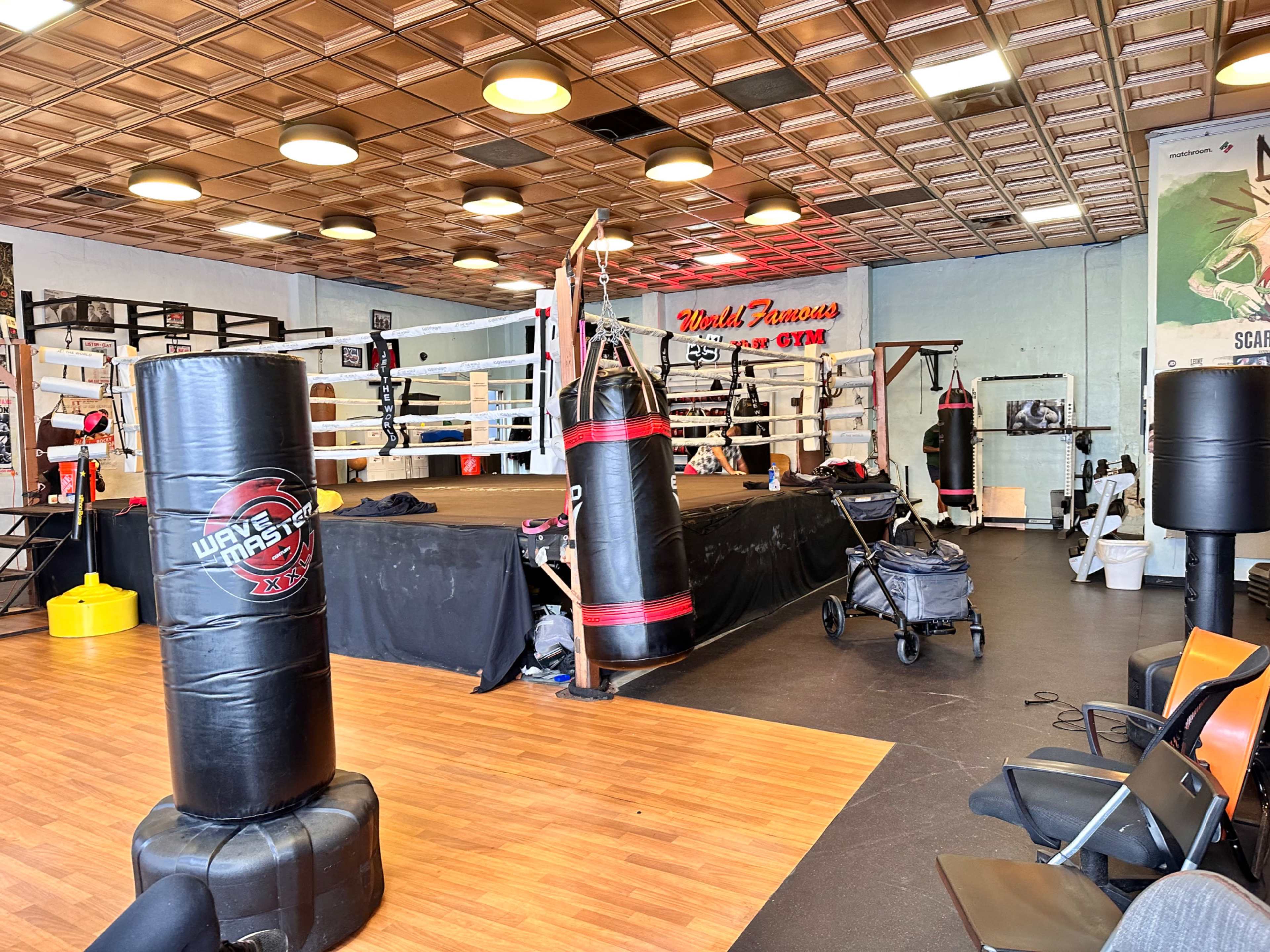 A boxing gym with a central ring, several punching bags, workout equipment, and seating areas.