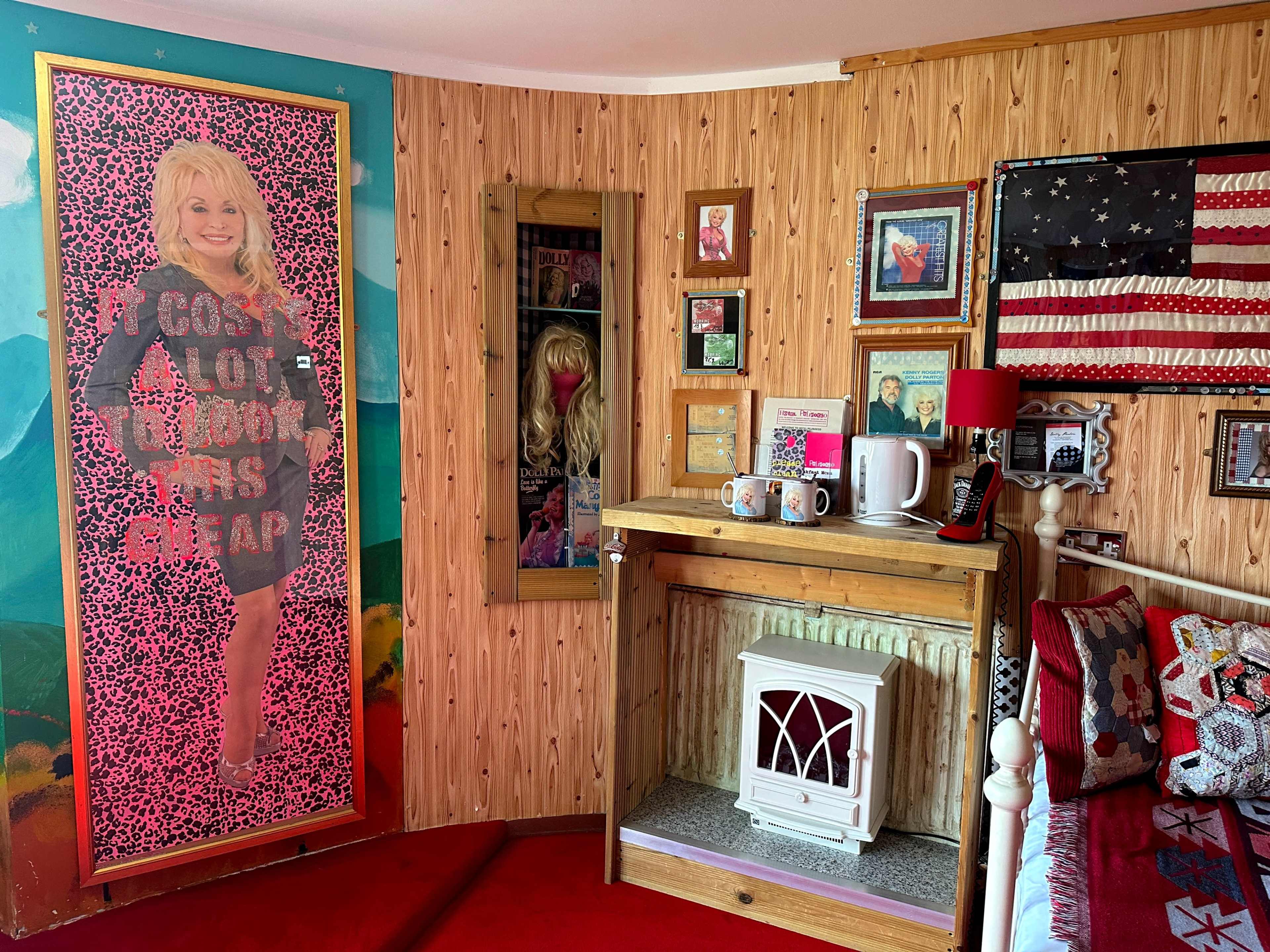 A room features a large poster of a smiling woman in a colorful outfit, surrounded by various framed pictures, an American flag, and a vintage-style heater.