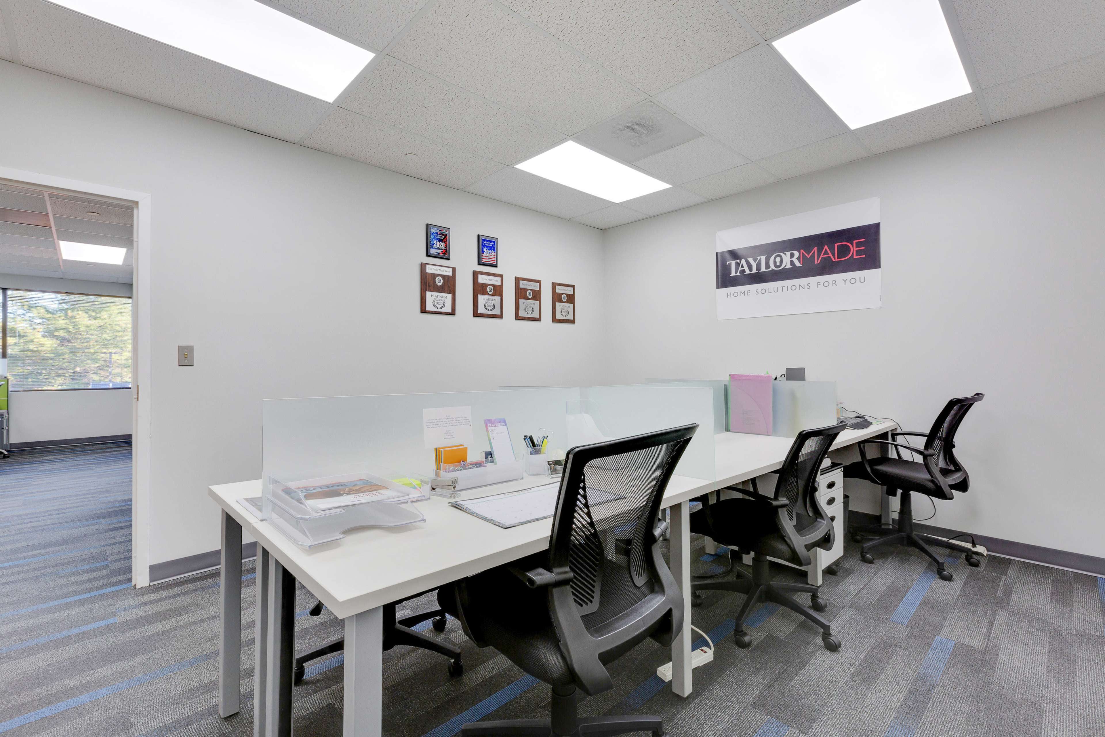 A modern office space with several desks, a wall displaying plaques, and a sign that reads "TAYLOR MADE."