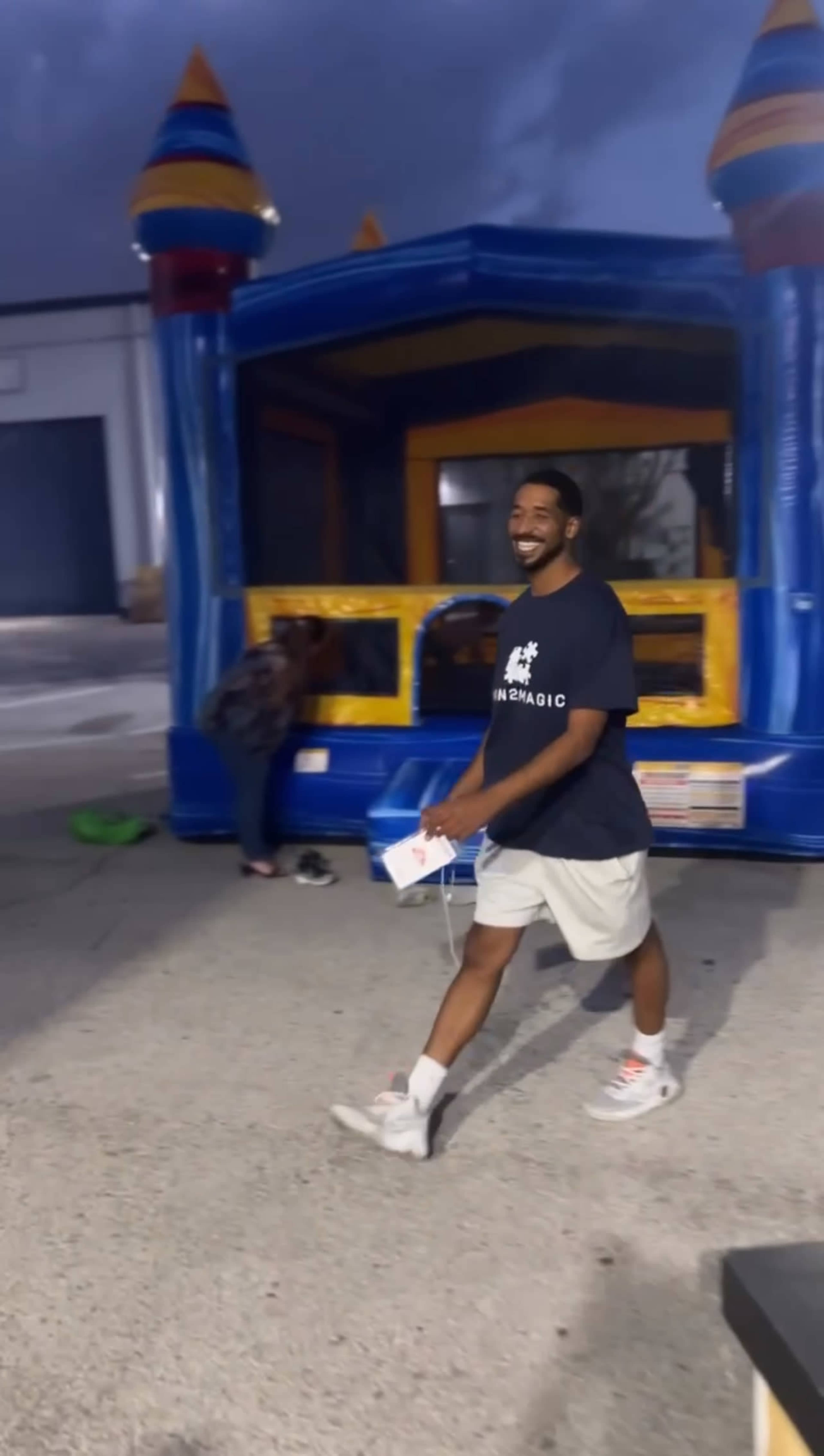 A man walks in front of a colorful bounce house while another person stands nearby.