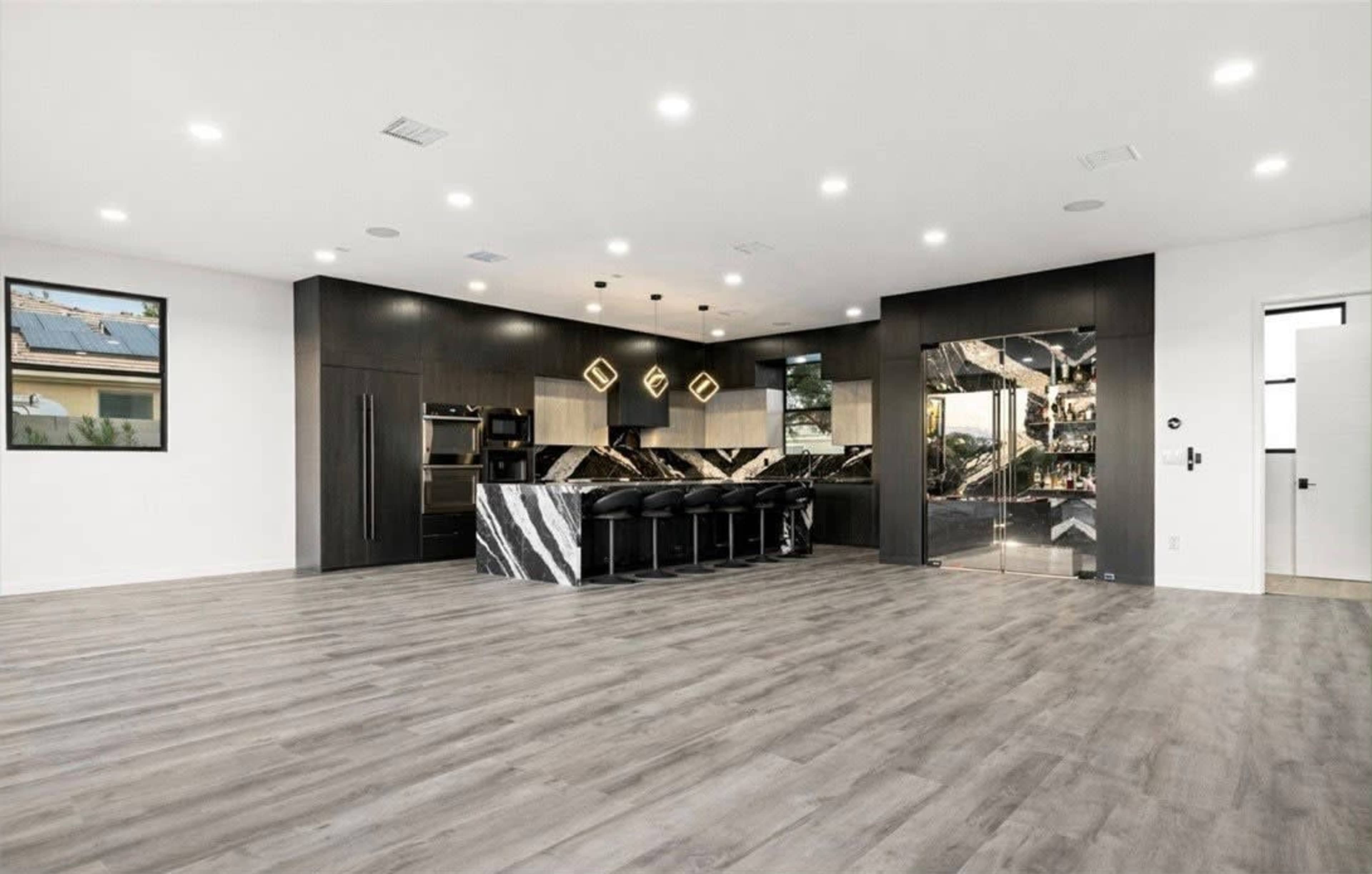 The image shows a modern kitchen with a black and white marble island, sleek cabinetry, and large, well-lit open space.