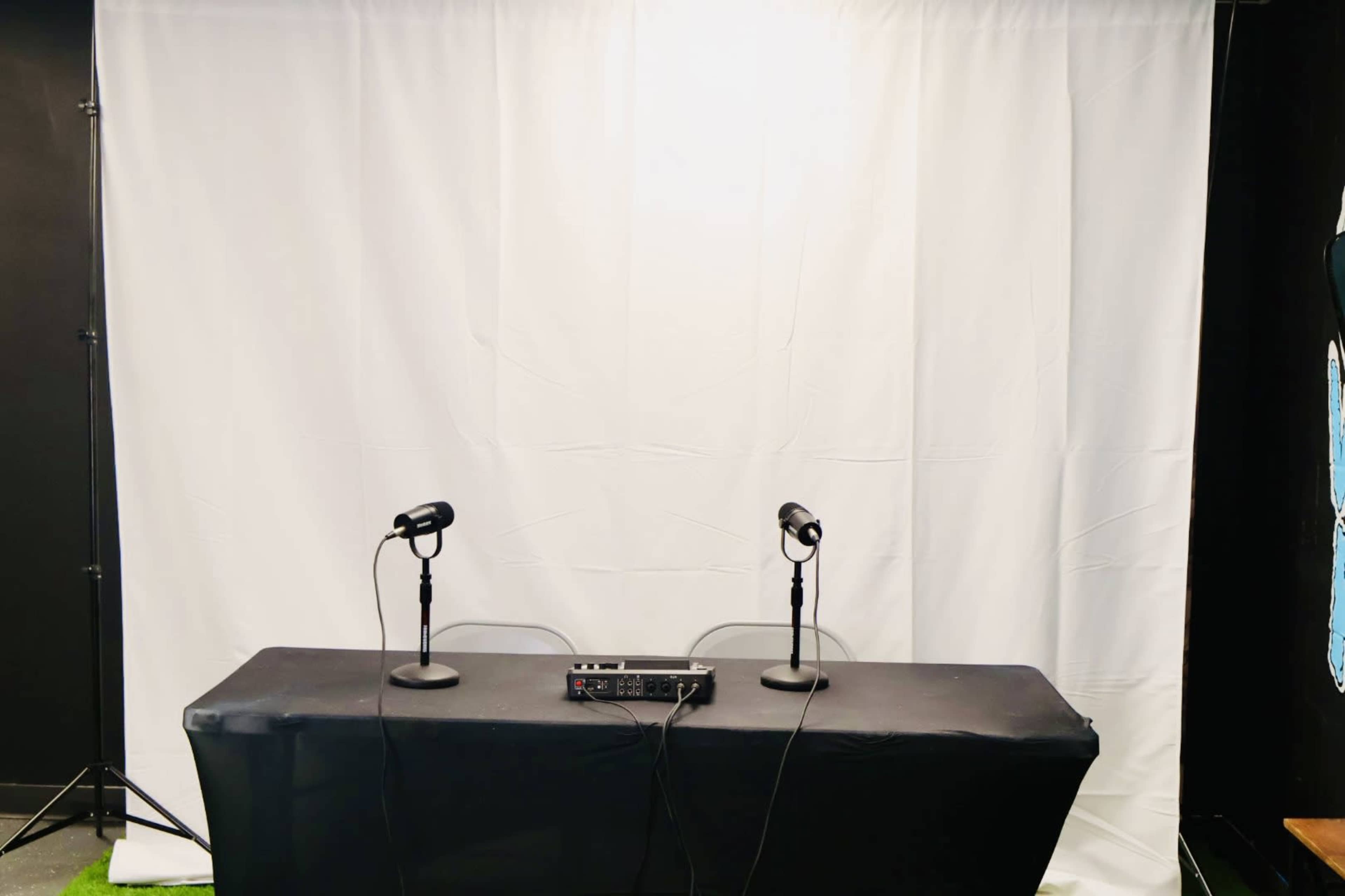 A black table with two microphones stands in front of a large white backdrop.