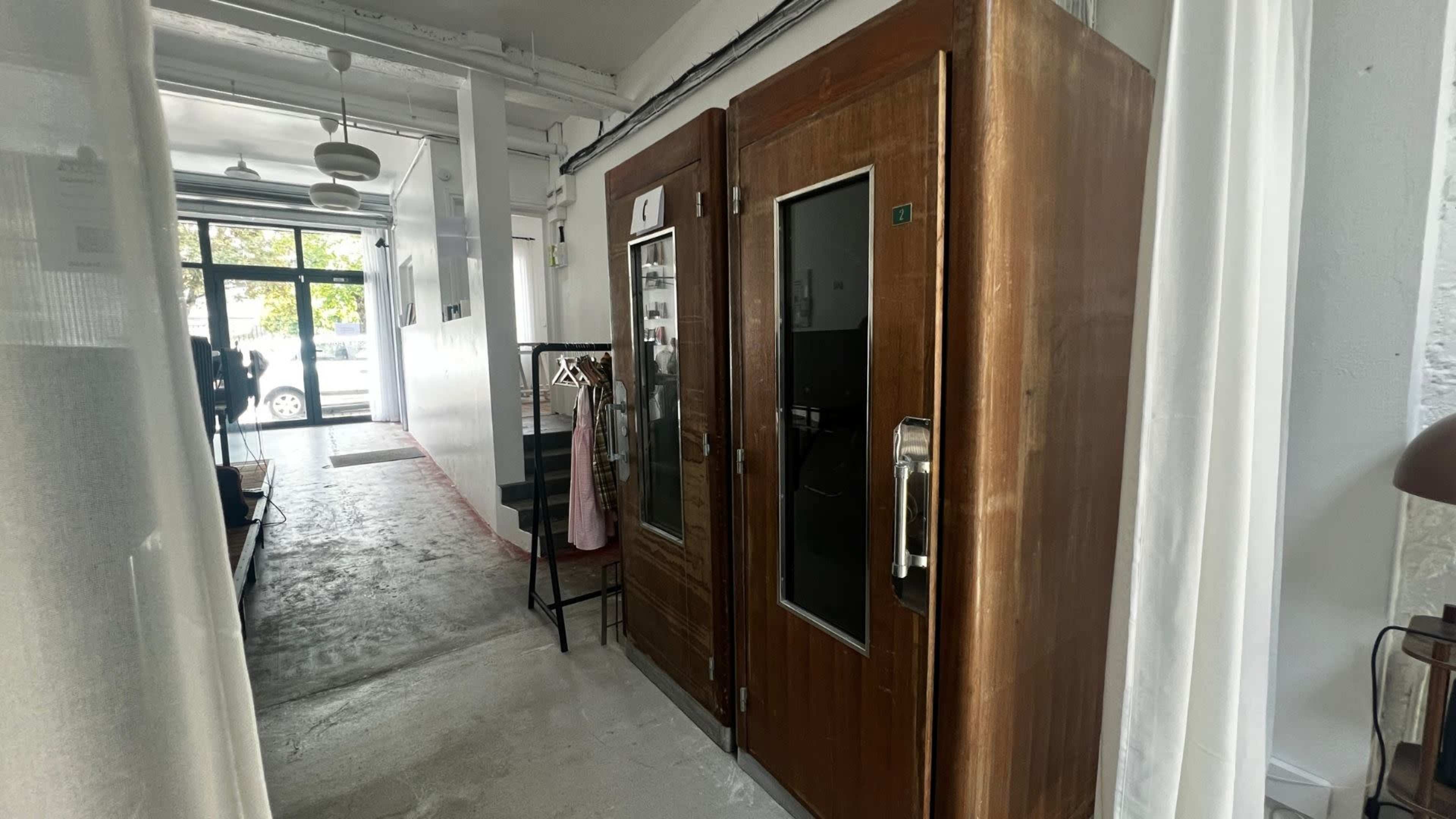 The image shows a narrow hallway with two wooden doors on the right and an open entrance at the far end leading outside.