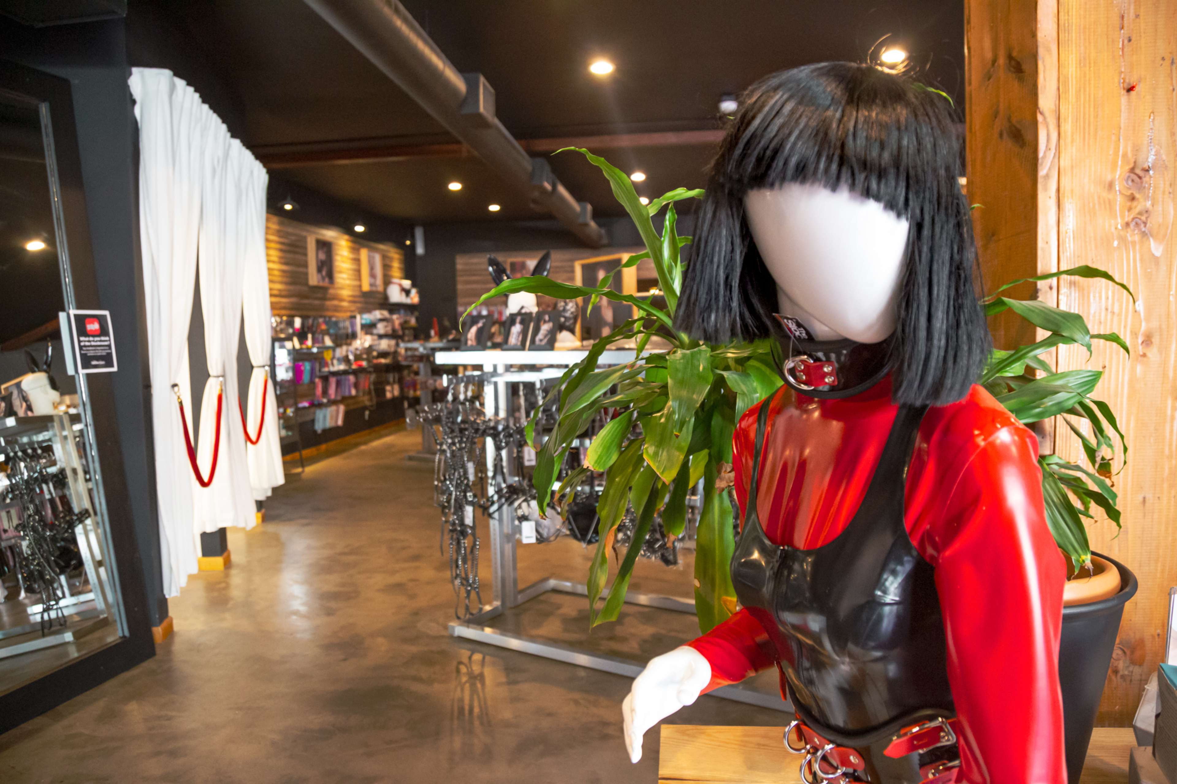 A mannequin dressed in a red and black outfit stands near a display of various items in a retail store.