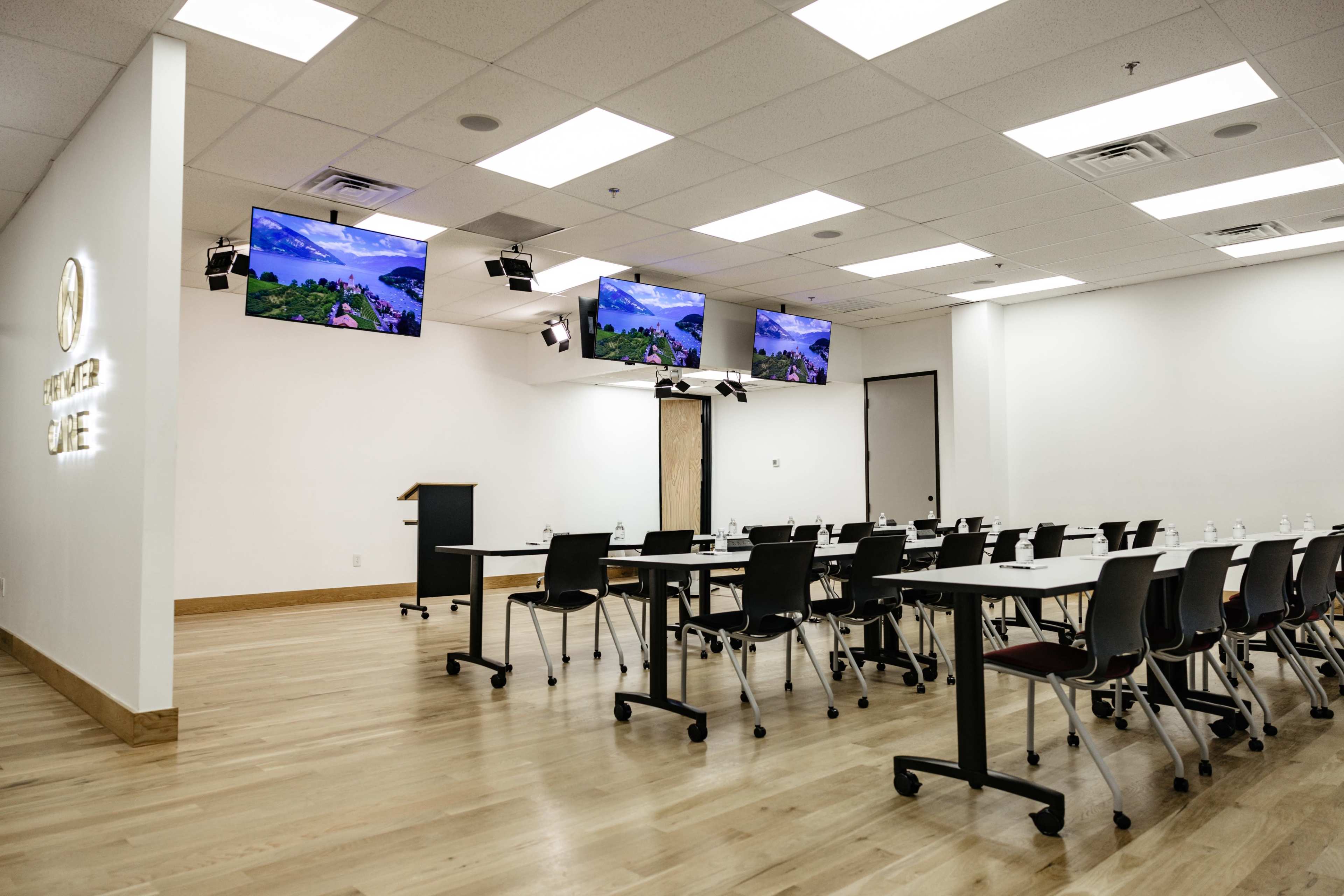 A modern conference room features multiple screens mounted on the walls and rows of tables arranged with chairs.