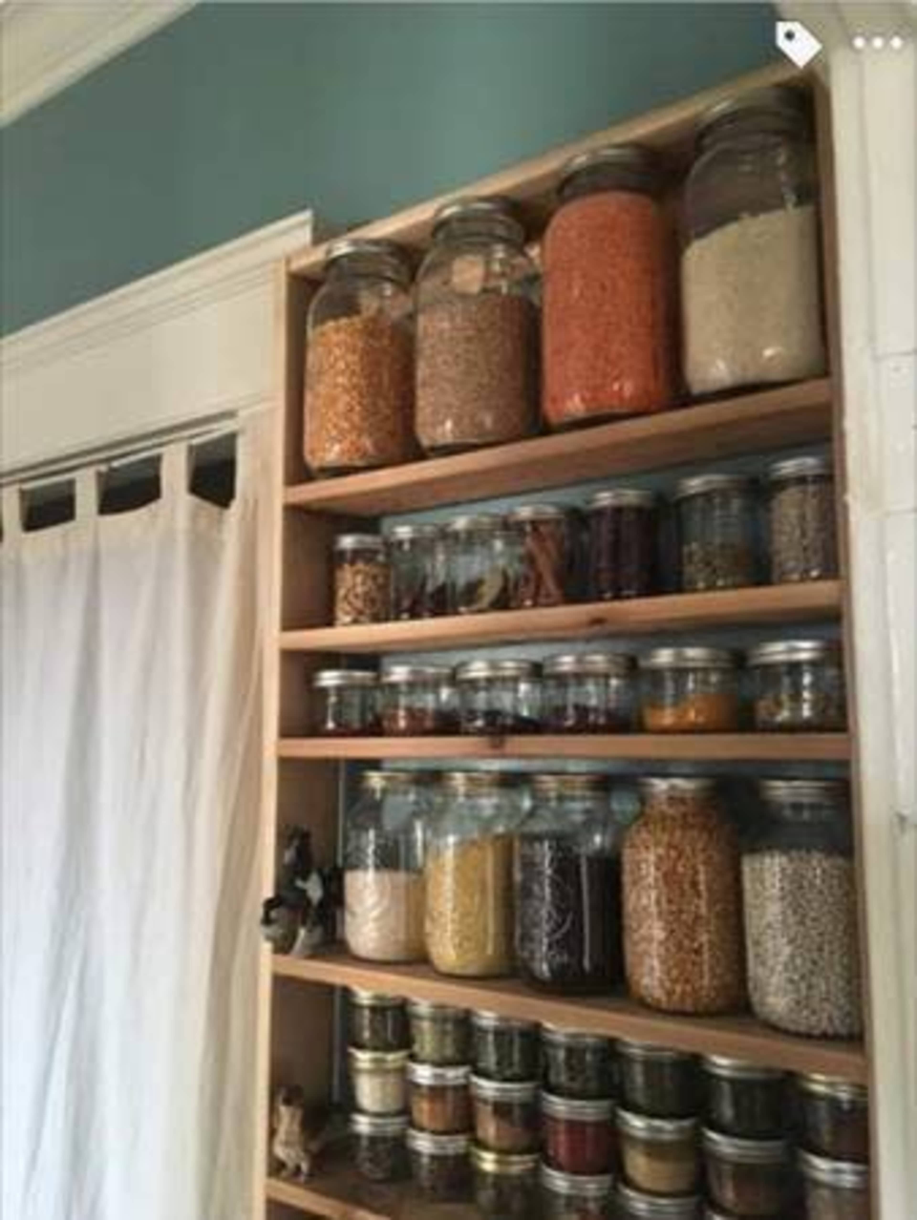 A wooden shelf filled with various glass jars containing colorful grains and spices, organized neatly against a muted wall.