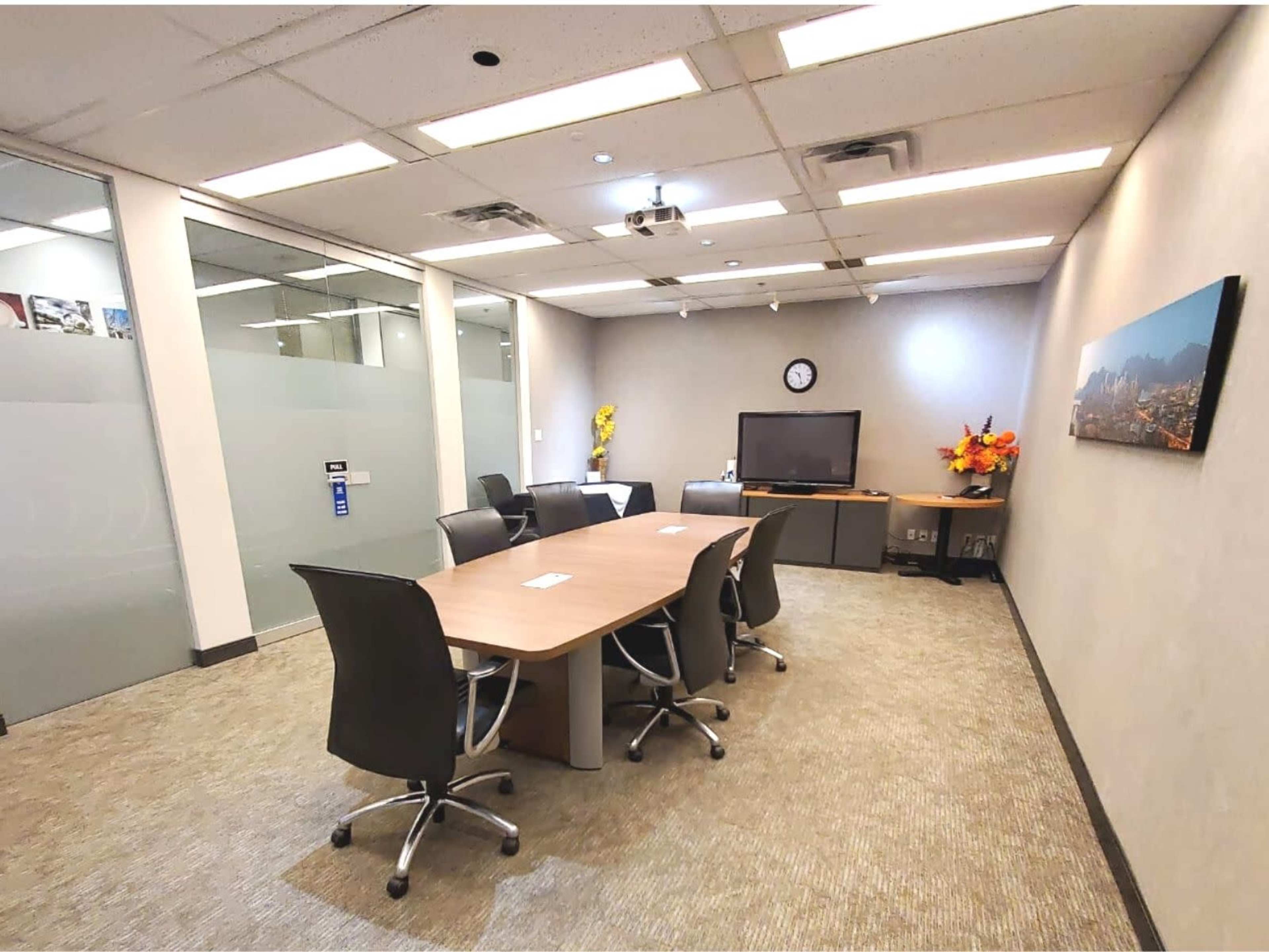 A modern conference room with a large table, ergonomic chairs, a television, and a wall clock.