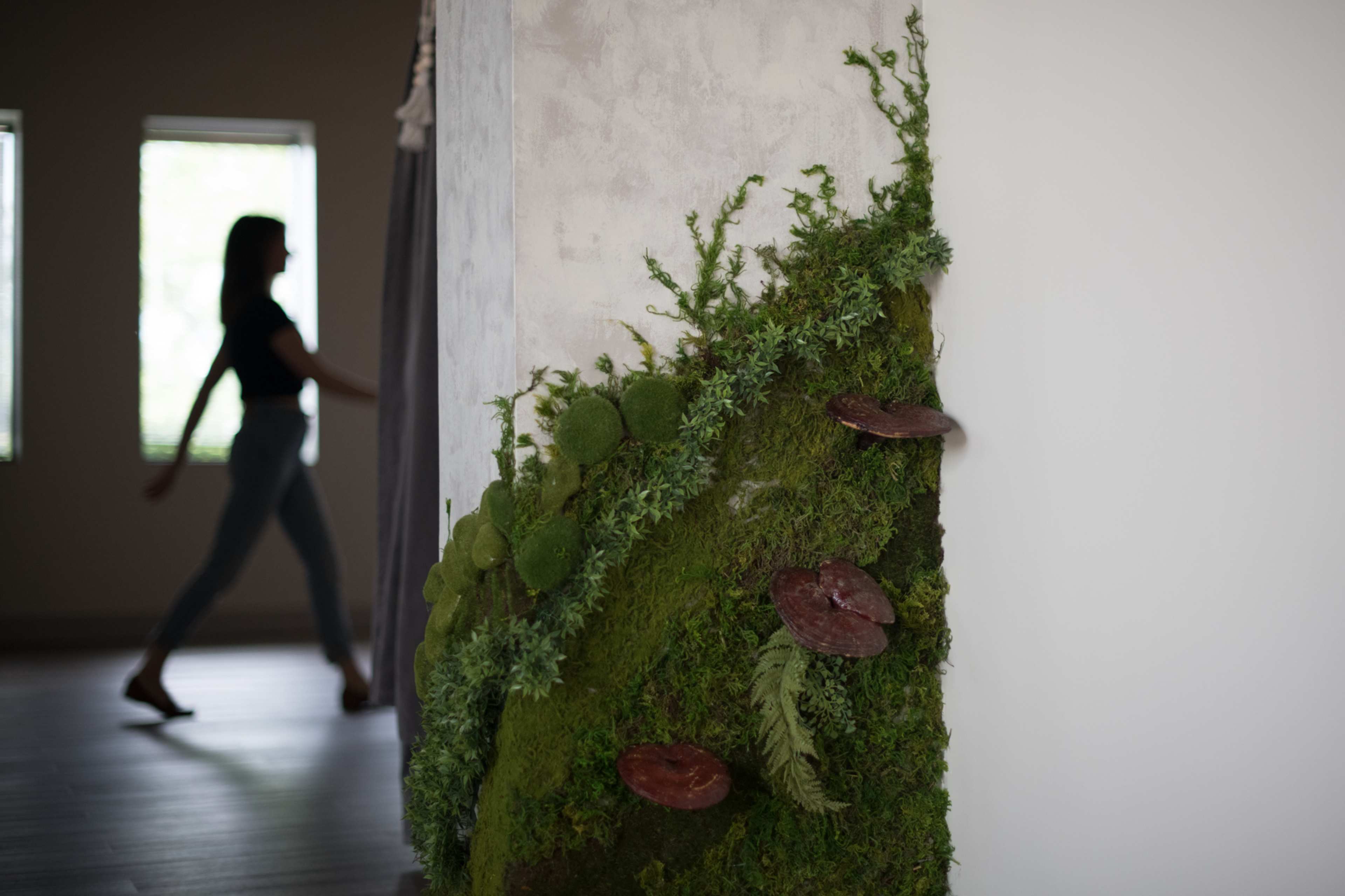 A person walks past a wall adorned with greenery and moss.
