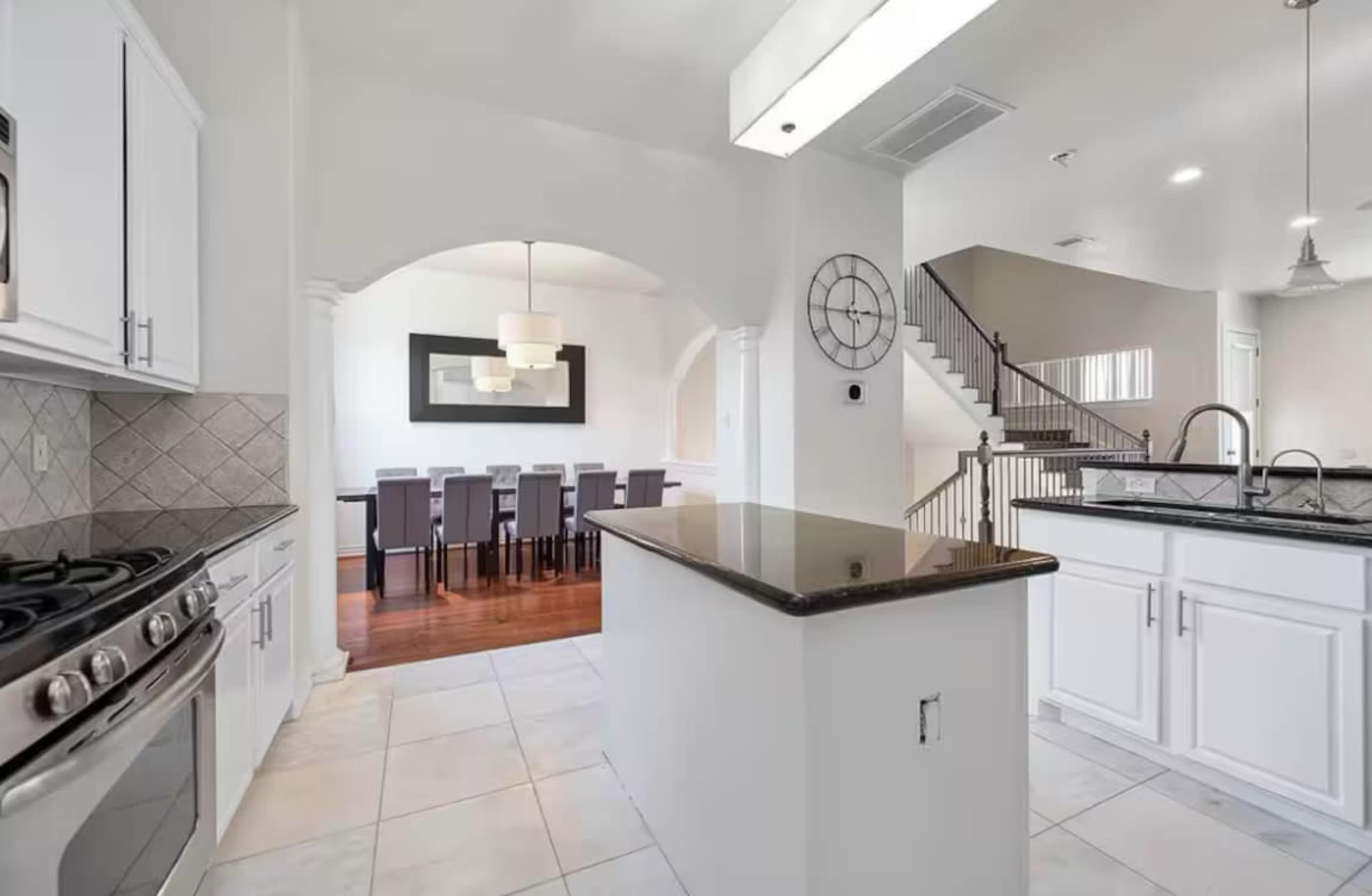 The image shows a modern kitchen with white cabinetry, a center island, and an adjacent dining area visible through an archway.
