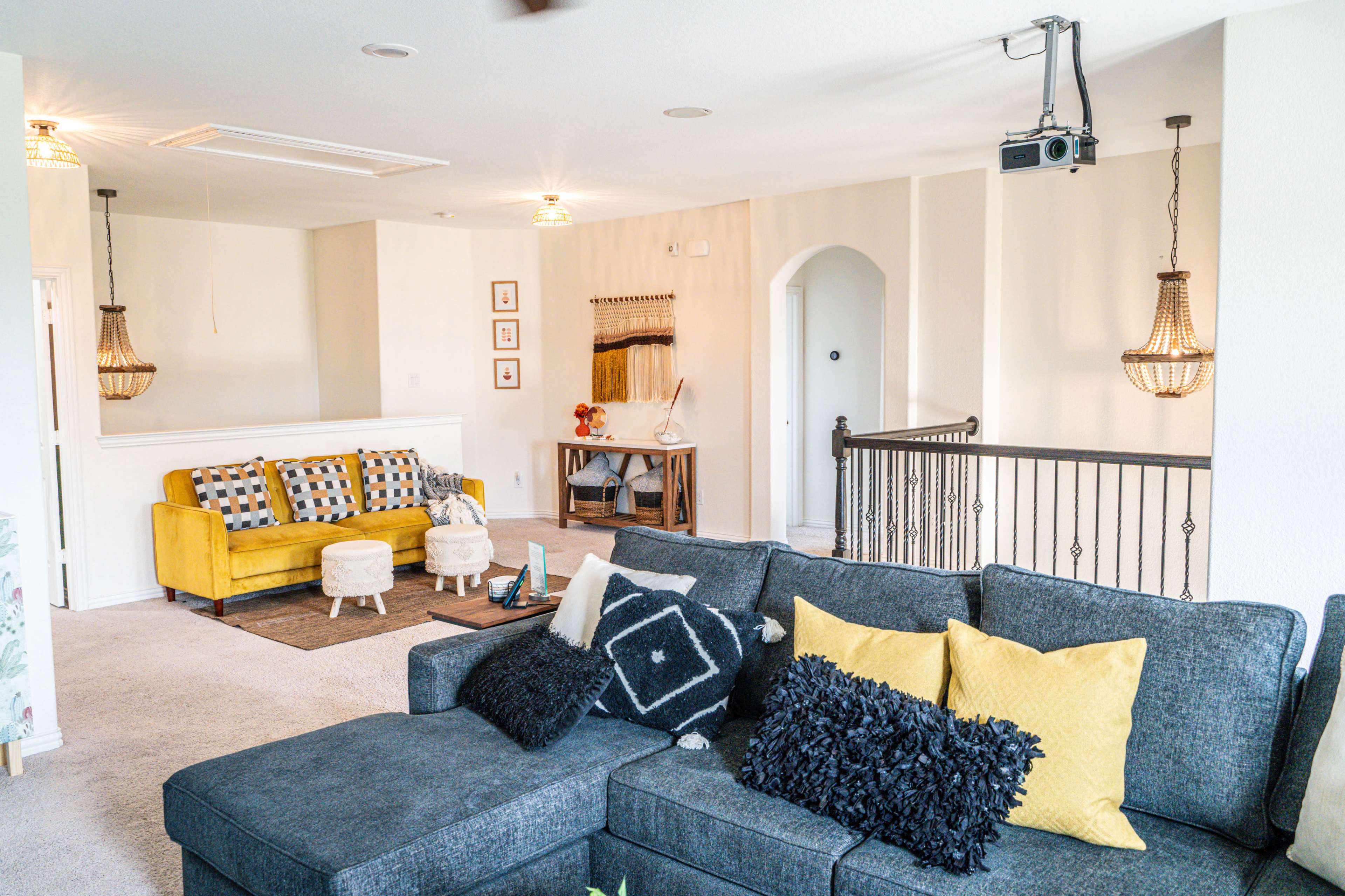 A bright living room with a gray sectional sofa, yellow accents, and a cozy decor featuring a projector, two chandeliers, and a rug.