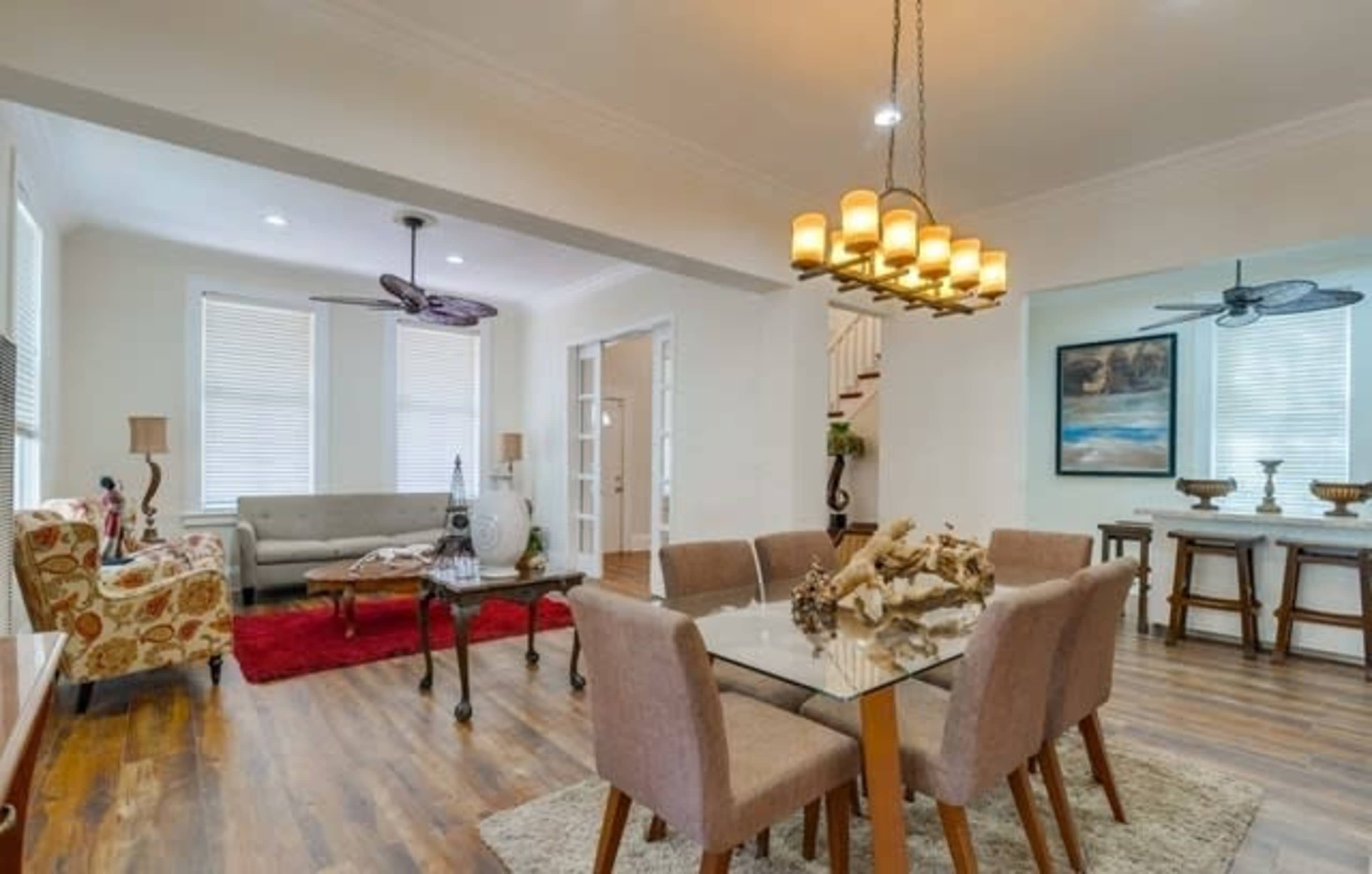 A modern living and dining area featuring a glass dining table, beige chairs, a comfortable sofa, and decorative lighting.