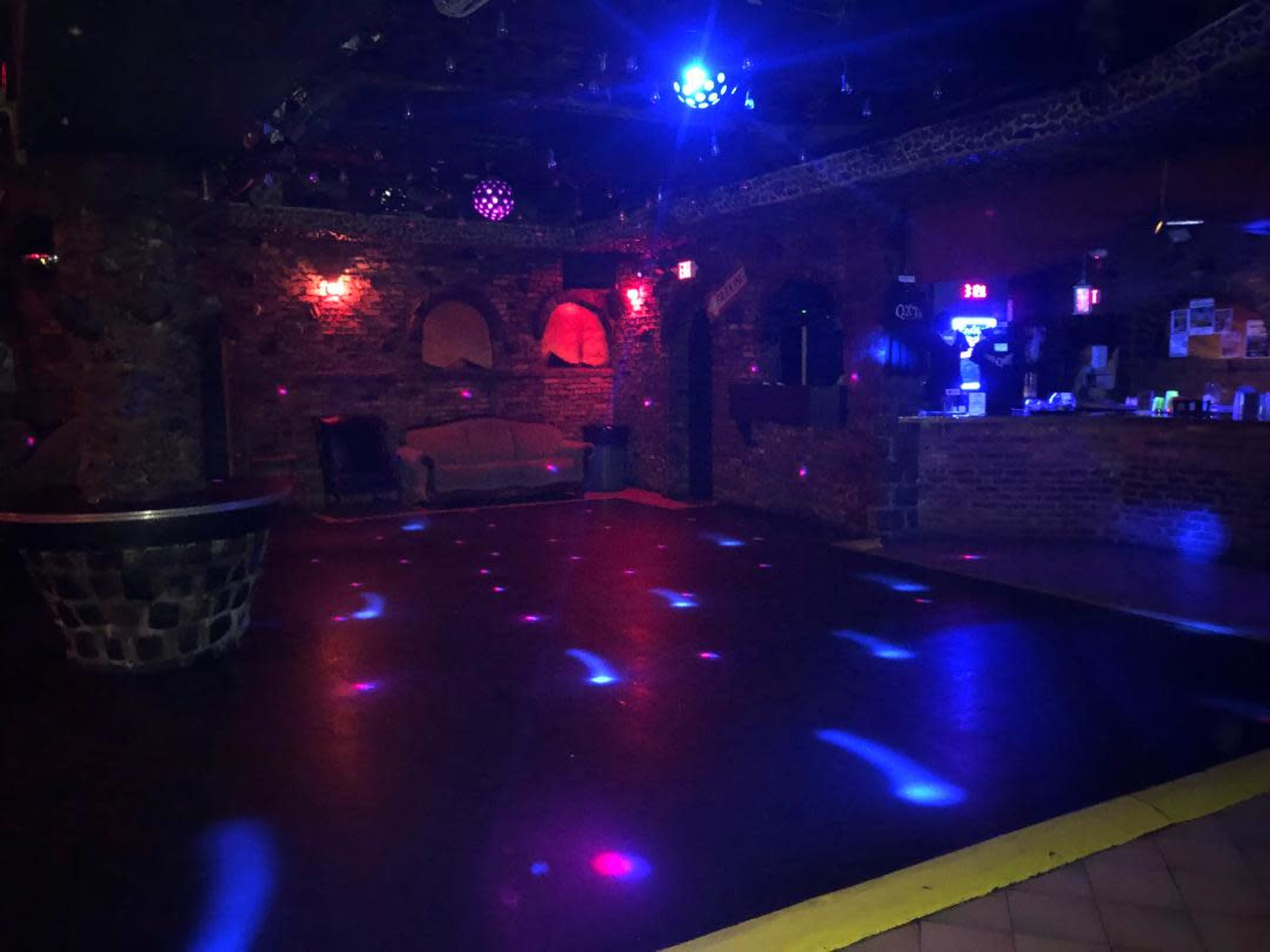 An empty dance floor in a dimly lit venue with brick walls and colorful light spots scattered across the floor.