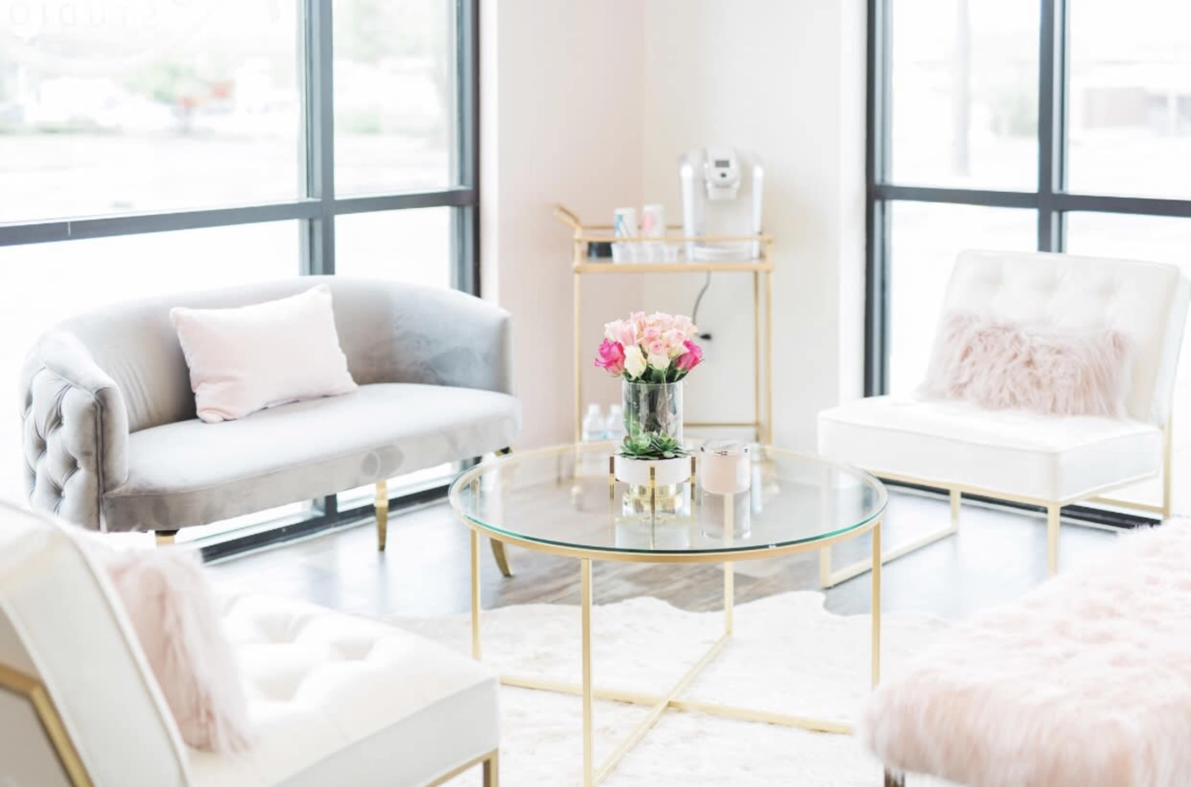 A modern waiting room featuring a glass coffee table surrounded by a gray couch and two white chairs, with a bouquet of flowers on the table.